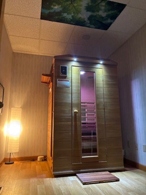 A wooden sauna with a glass door and control panel, illuminated by warm lighting, in a room with wooden flooring.