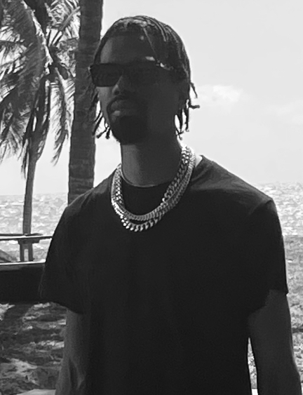 Person wearing sunglasses and jewelry, standing outdoors with palm trees in the background.