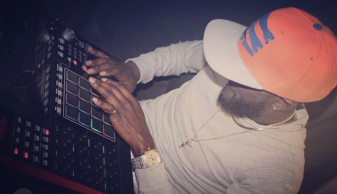 Person wearing a white hoodie and orange cap using a DJ controller in a dark environment.