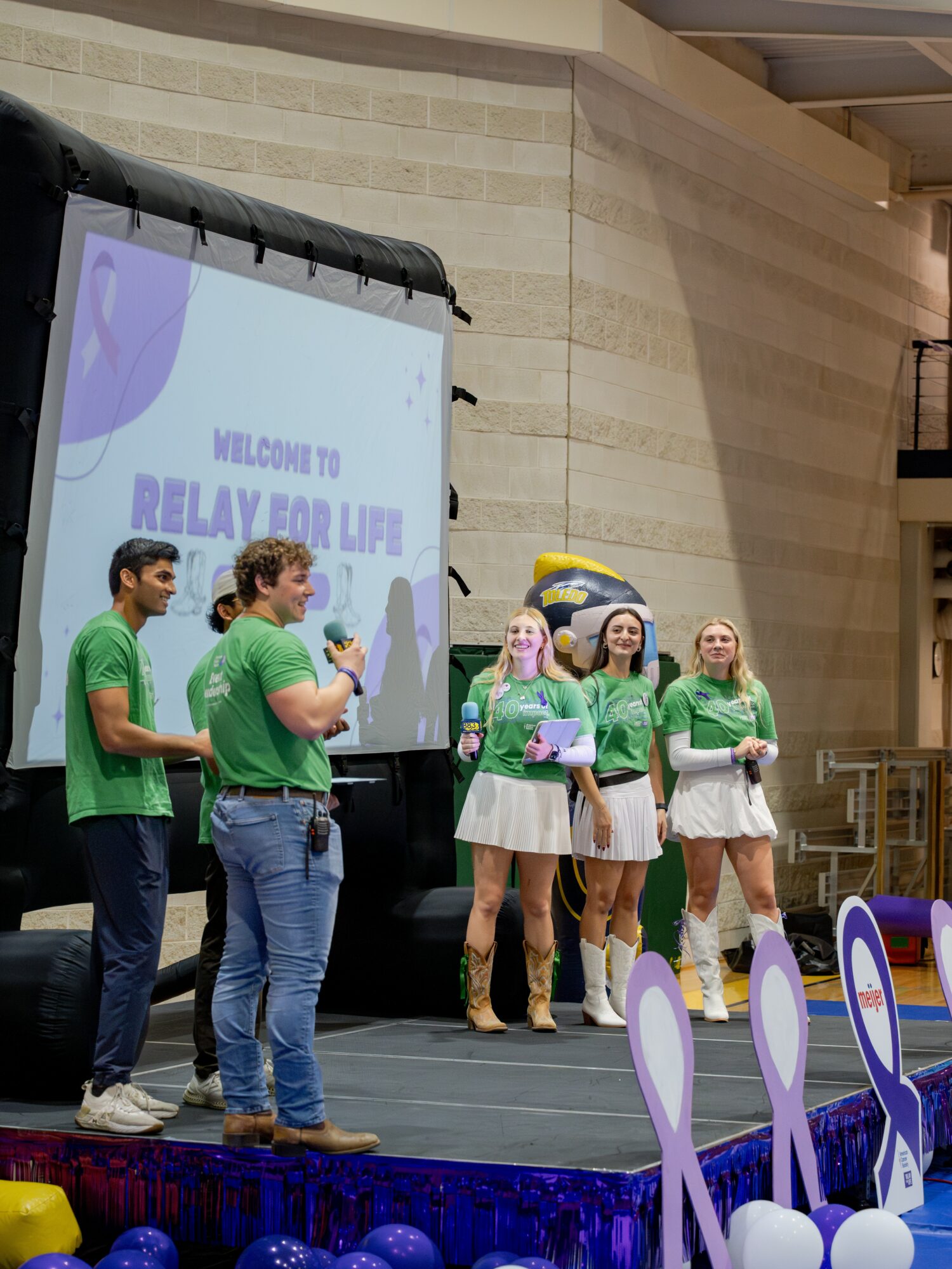 Group of people on stage with a screen displaying 'Welcome to Relay for Life' in a large indoor venue.