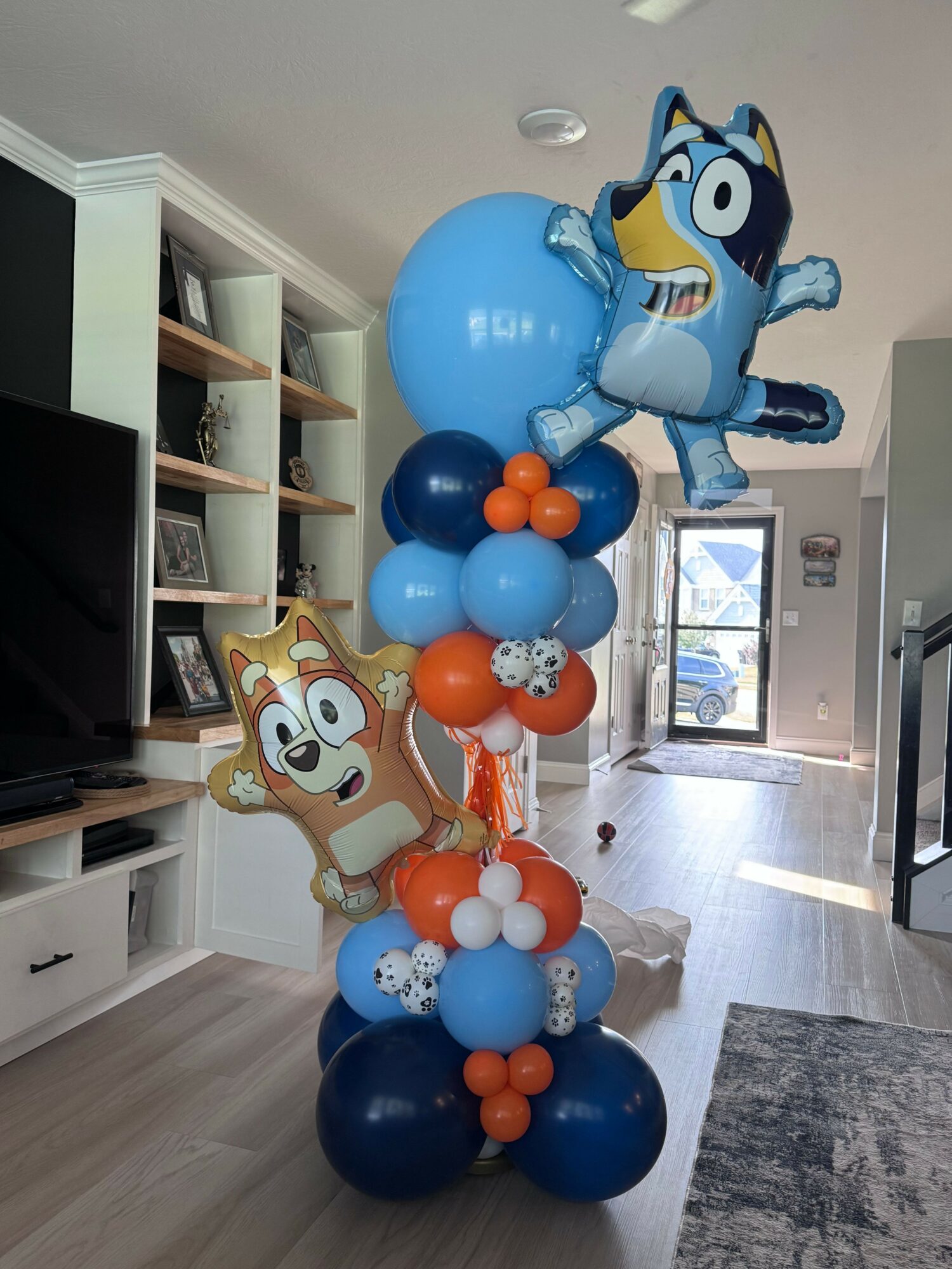 Party decorations with blue, orange, and white balloons, and character cutouts in a room with a door and window.