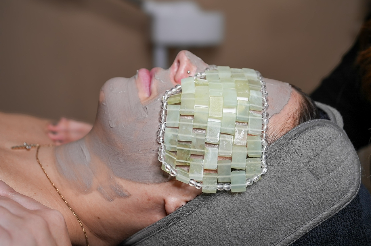 Person lying down with a facial mask and a woven eye mask, resting on a pillow.