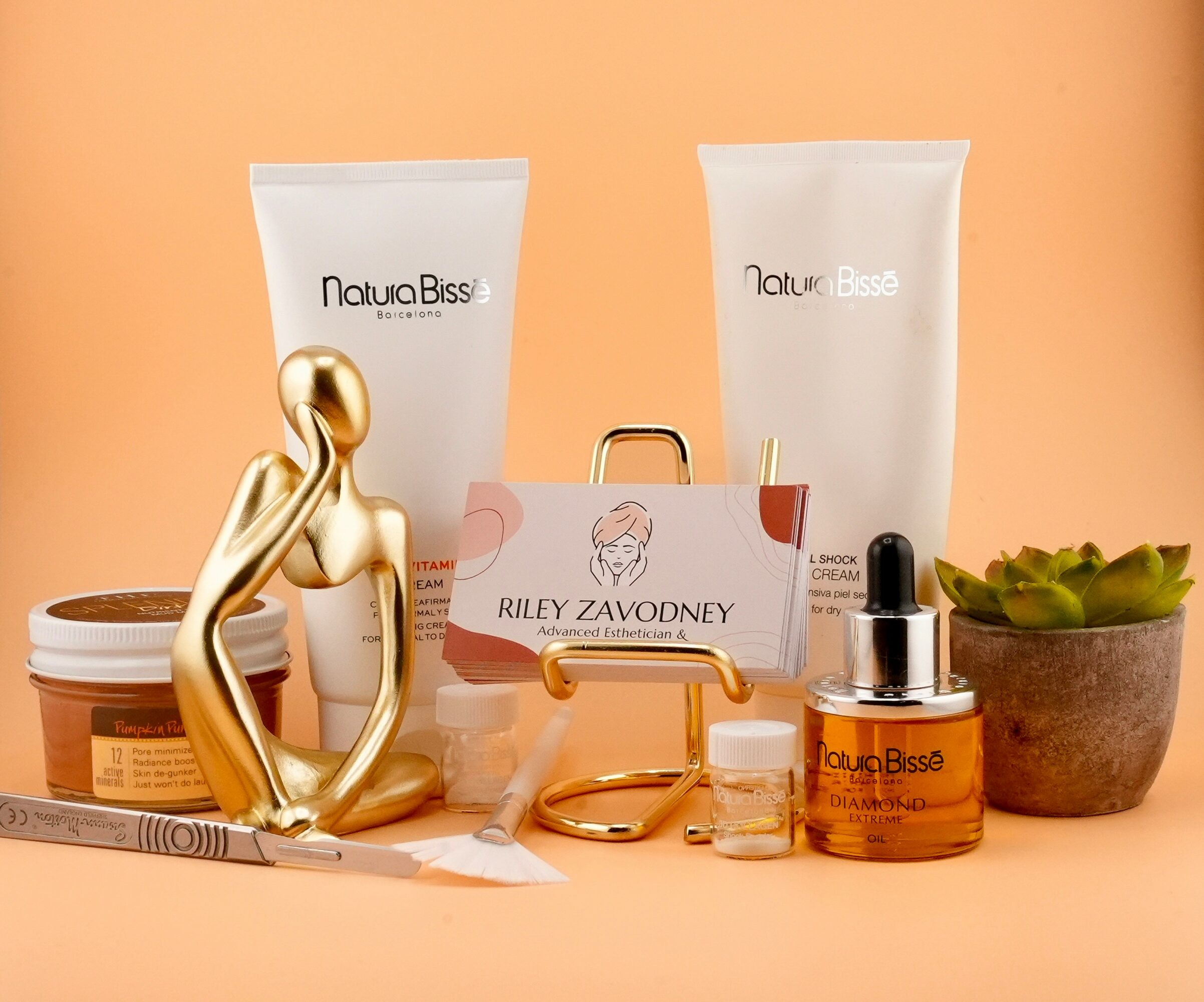 Arrangement of skincare products, a gold sculpture, and a business card on a peach background.