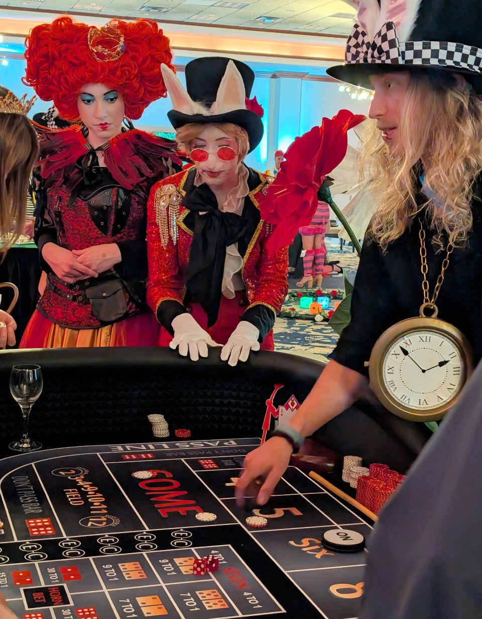 Three people dressed as characters from Alice in Wonderland playing roulette at a casino table, with a clock on the table.