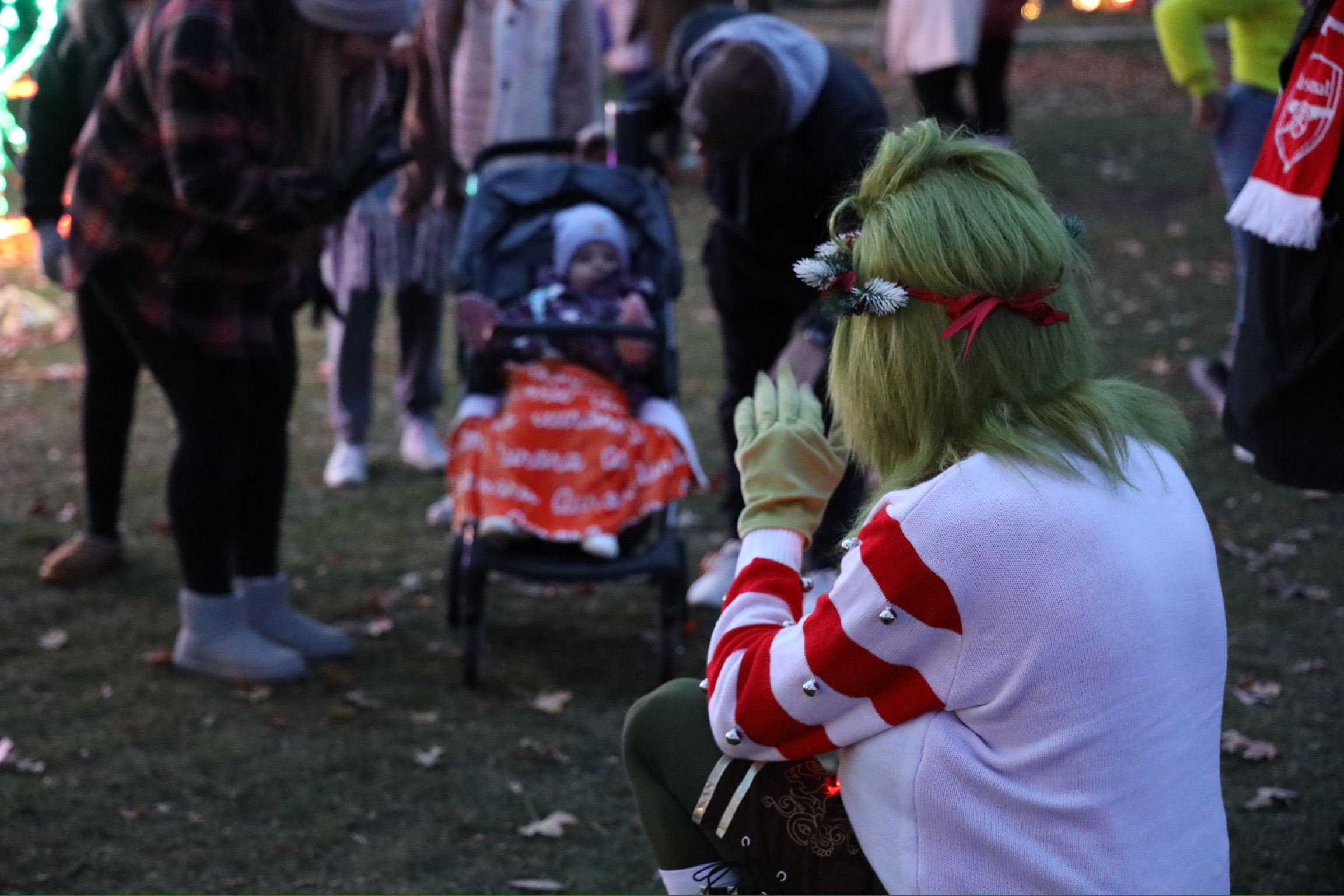Person with green hair and a red headband sitting outdoors, surrounded by people and a stroller, during evening light.