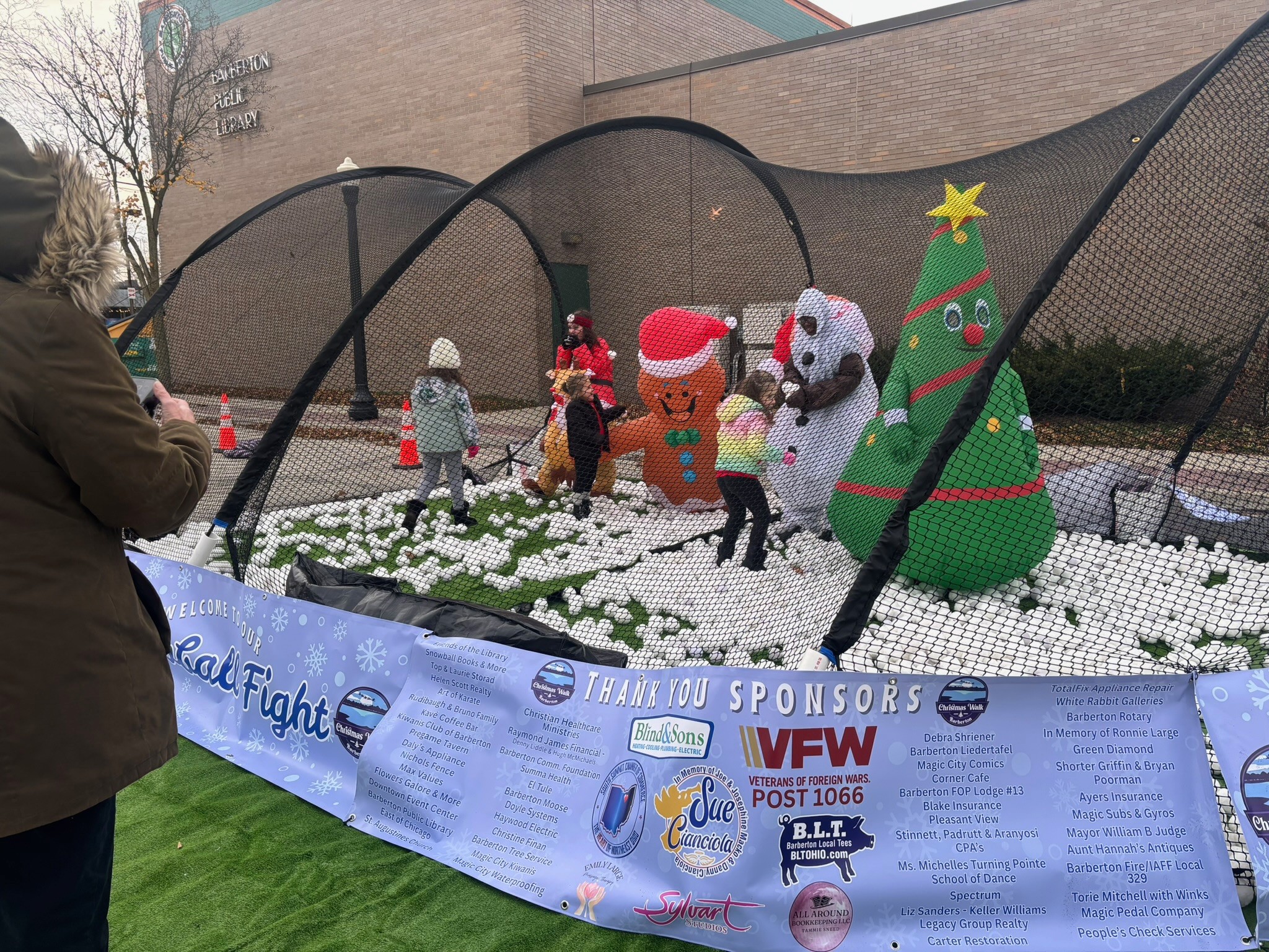 Inflatable Christmas decorations including a tree, snowman, gingerbread man, and a dog, with children and adults nearby, in a garden area.