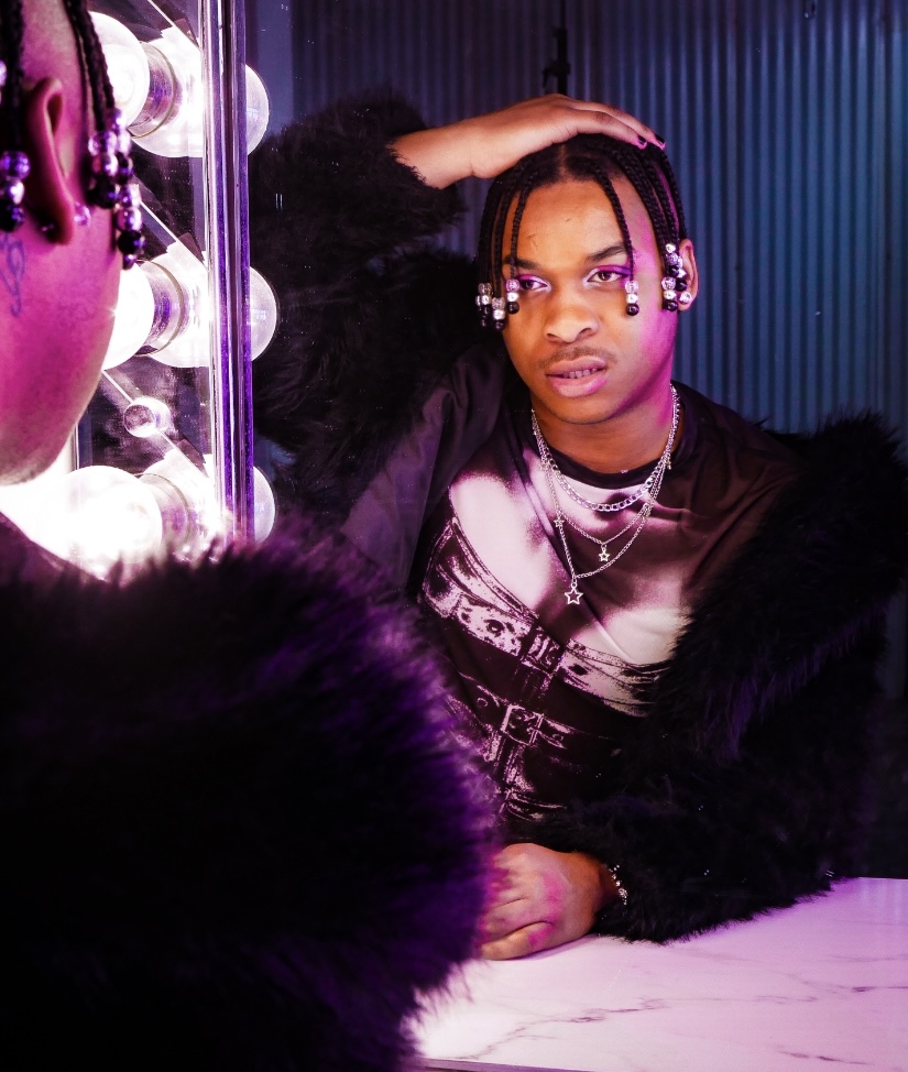 Woman with braided hair and jewelry, sitting at a table with colorful lighting and a mirror with lights.
