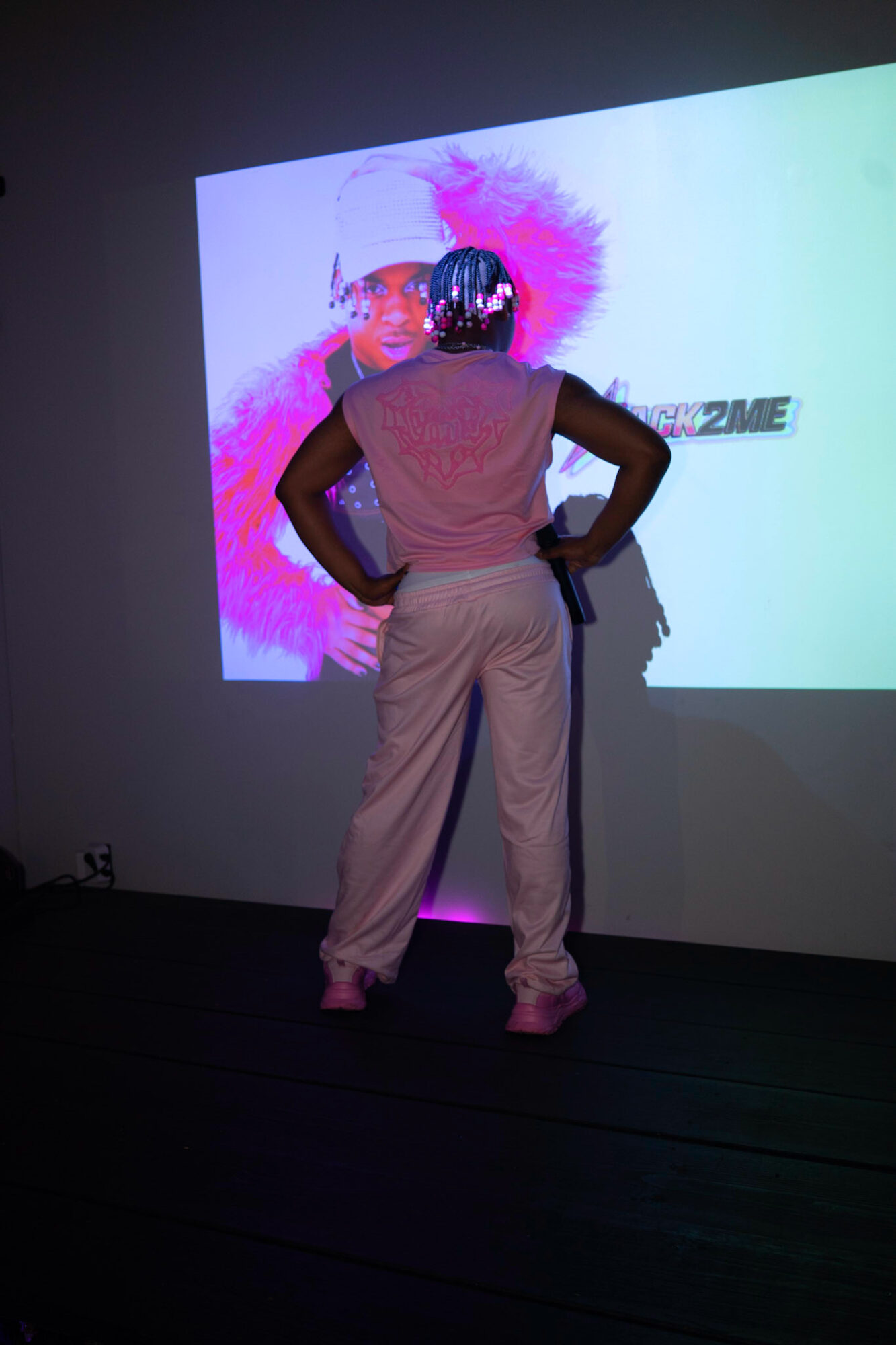 Person standing with hands on hips facing a large screen displaying colorful graphics and text.