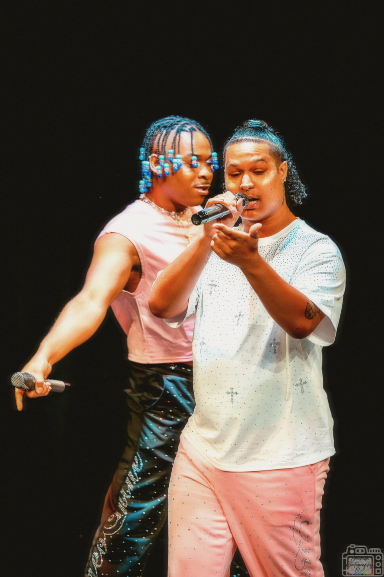 Two women stand close together, one showing something on a phone to the other, against a dark background.