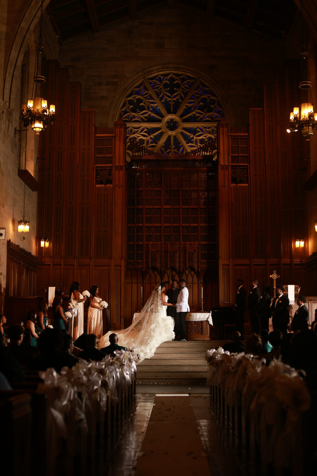 Wedding ceremony inside a church with a bride, groom, and officiant at the altar, guests seated, ornate wooden interior, stained glass window.