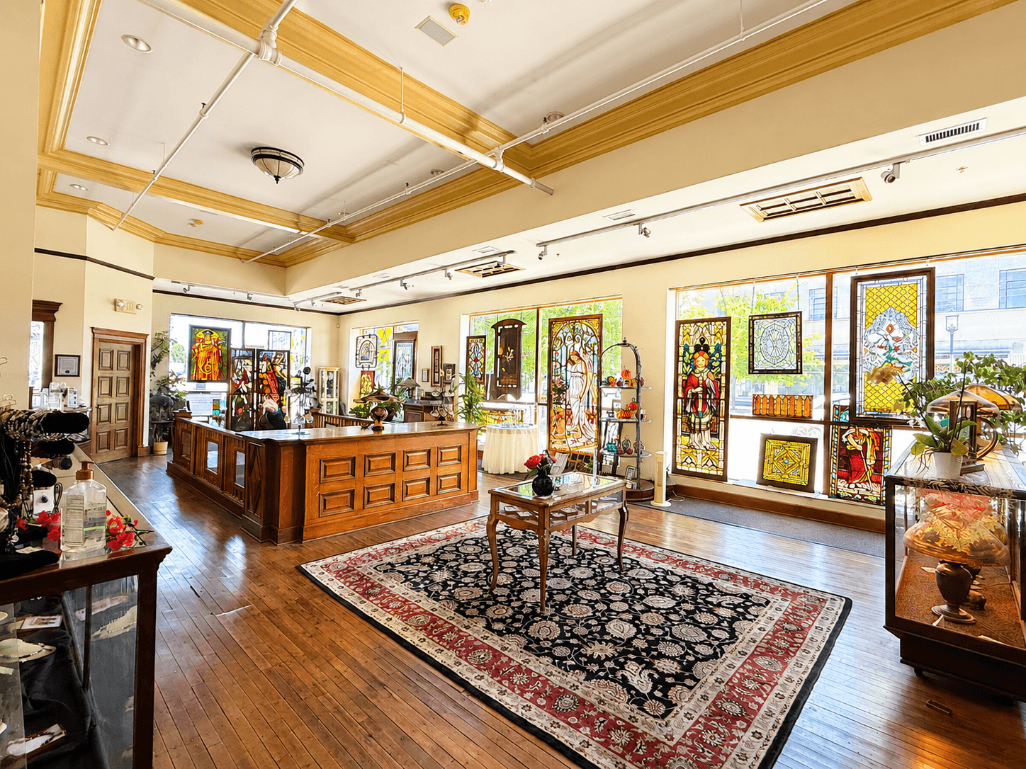 Room with large windows, wooden furniture, decorative items, and a patterned rug on hardwood floor.