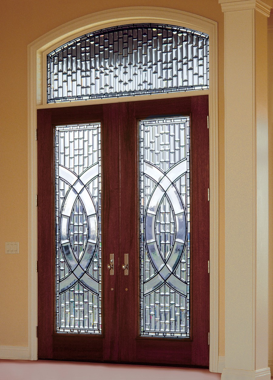 Double wooden door with decorative glass panels and a transom window above, set in a yellow wall.