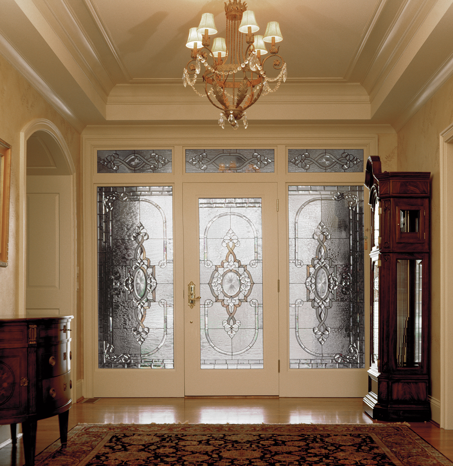 Elegant entryway with glass doors, chandelier, and antique furniture, featuring a patterned rug and decorative glass panels.