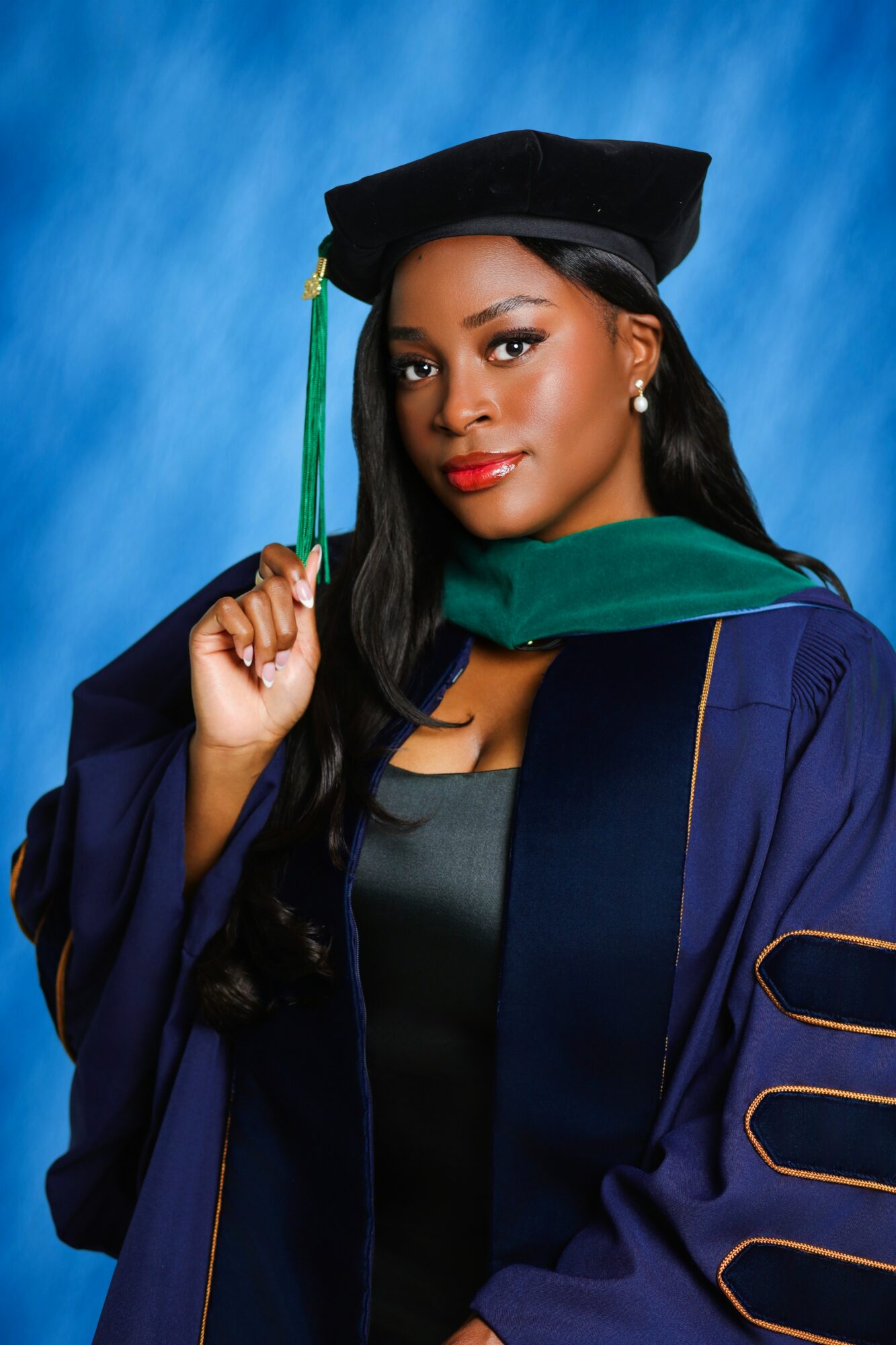 Woman in graduation gown and cap holding tassel, smiling, against blue background.