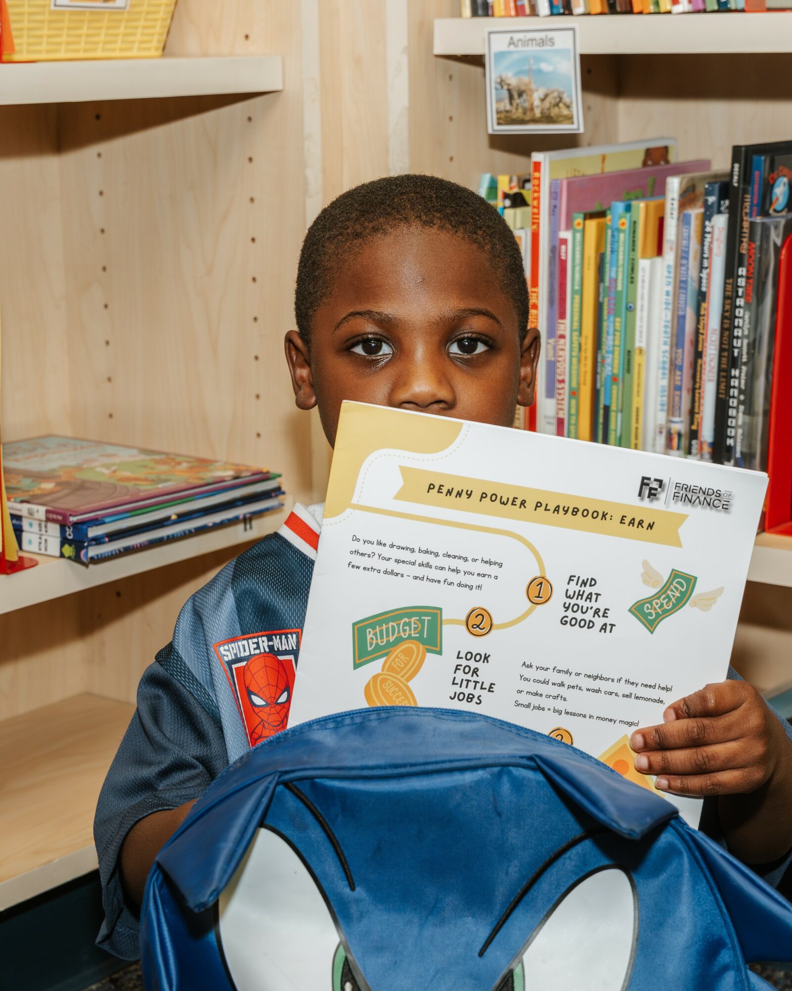 Child holding a worksheet in a library, with bookshelves in the background.