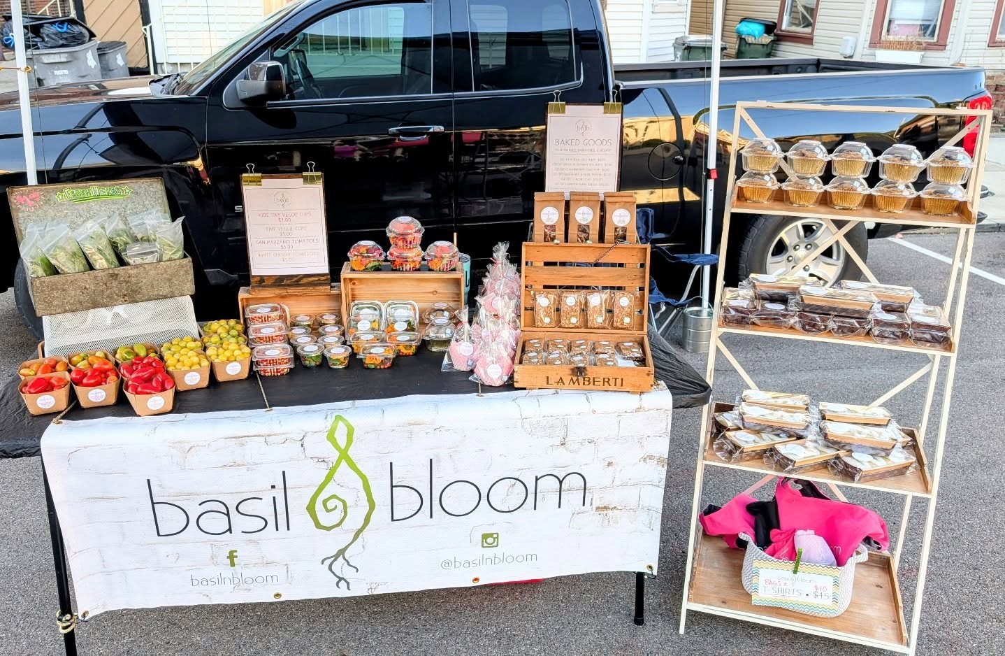 Market stall with jars of food, a sign reading 'basil & bloom,' and a black vehicle in the background.