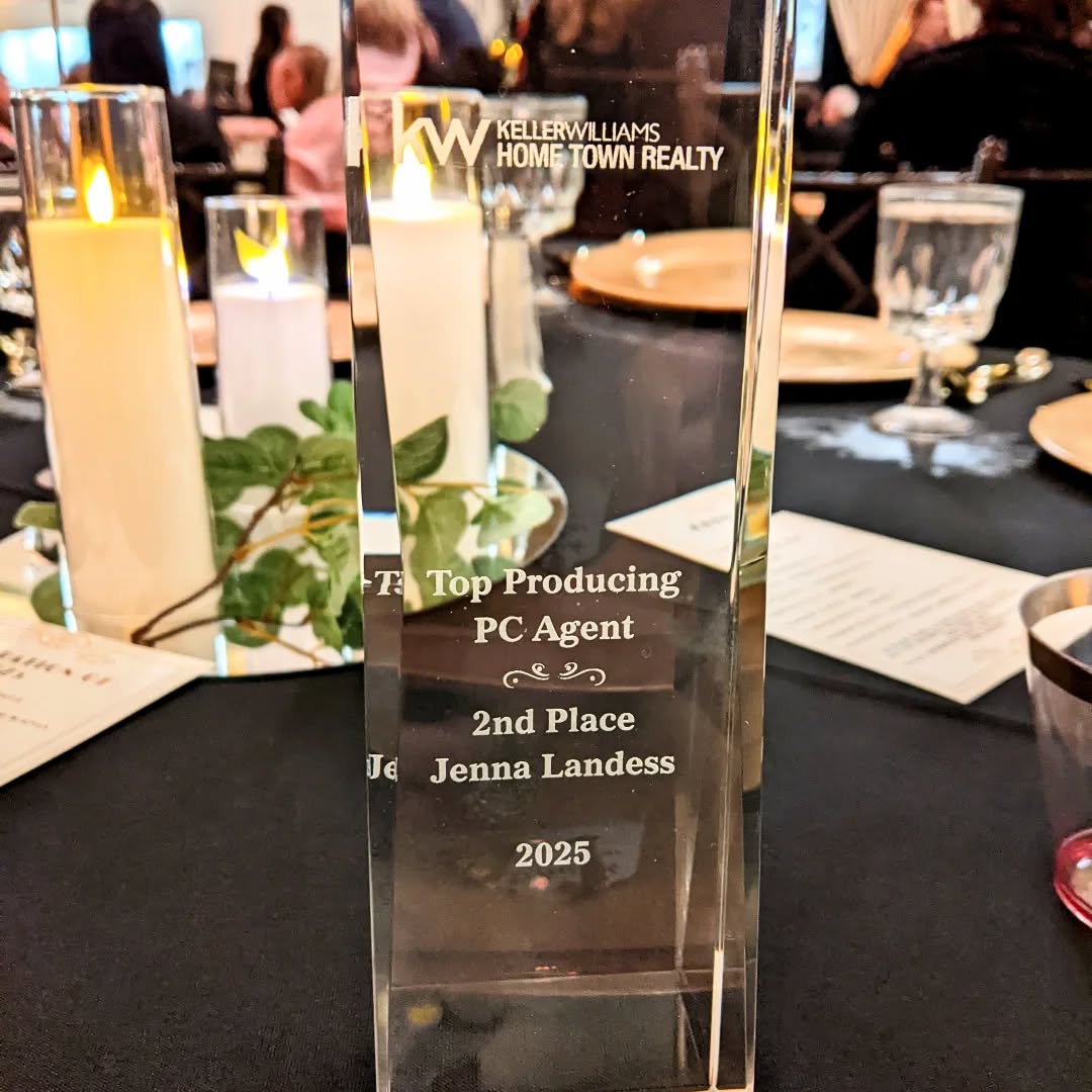 Clear glass award with text, on a table with candles and tableware, at an indoor event.