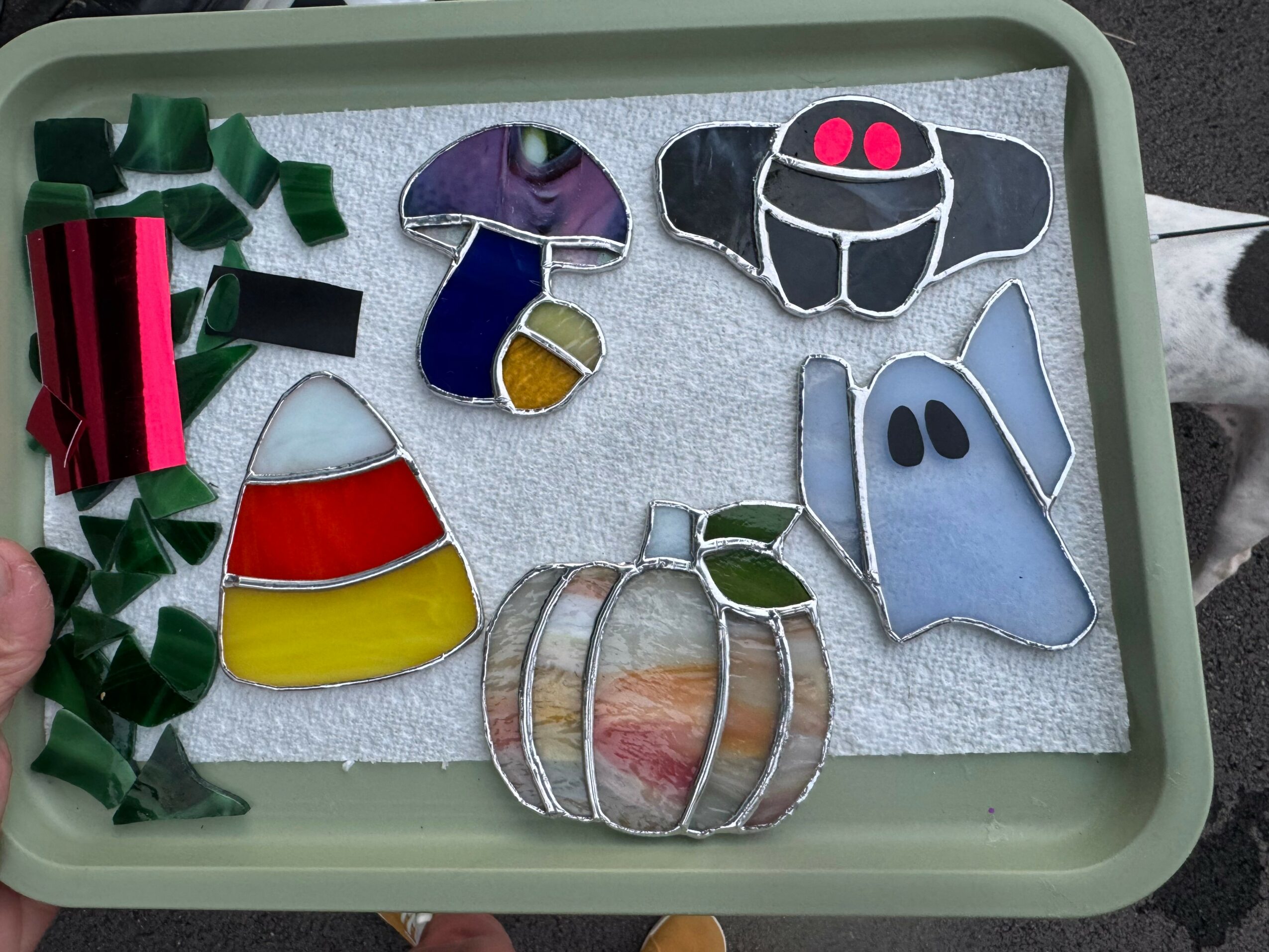 Decorative ornaments on a tray, including a pumpkin, ghost, and colorful shapes, with green ribbon on the side.