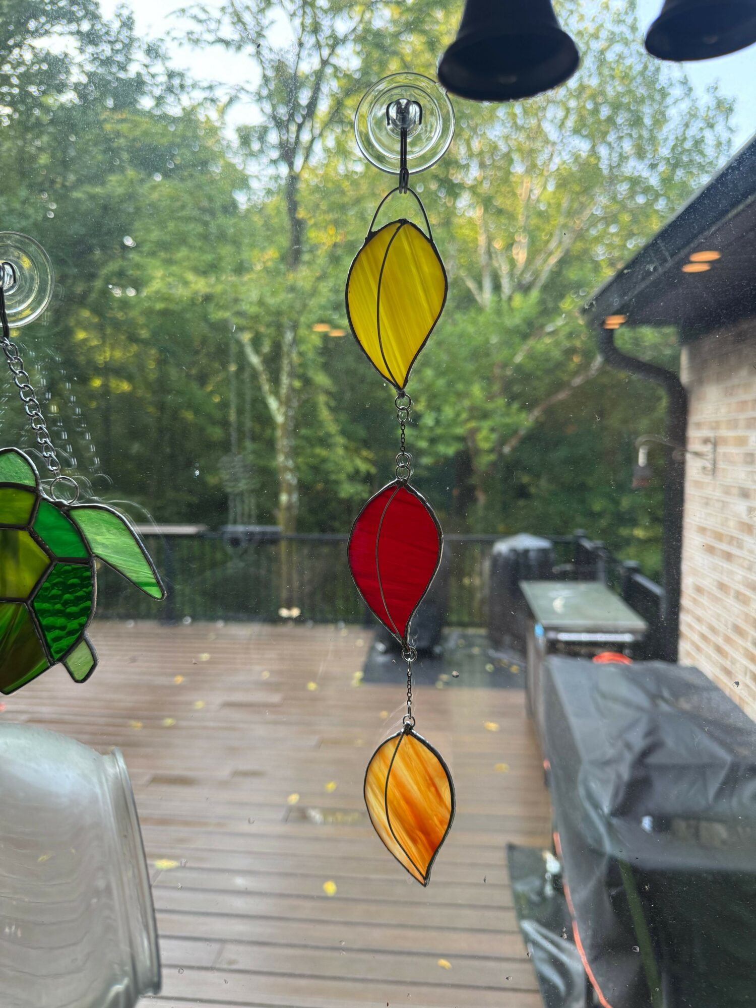 Colorful leaf-shaped wind chimes hanging outdoors with trees and a wooden deck in the background.