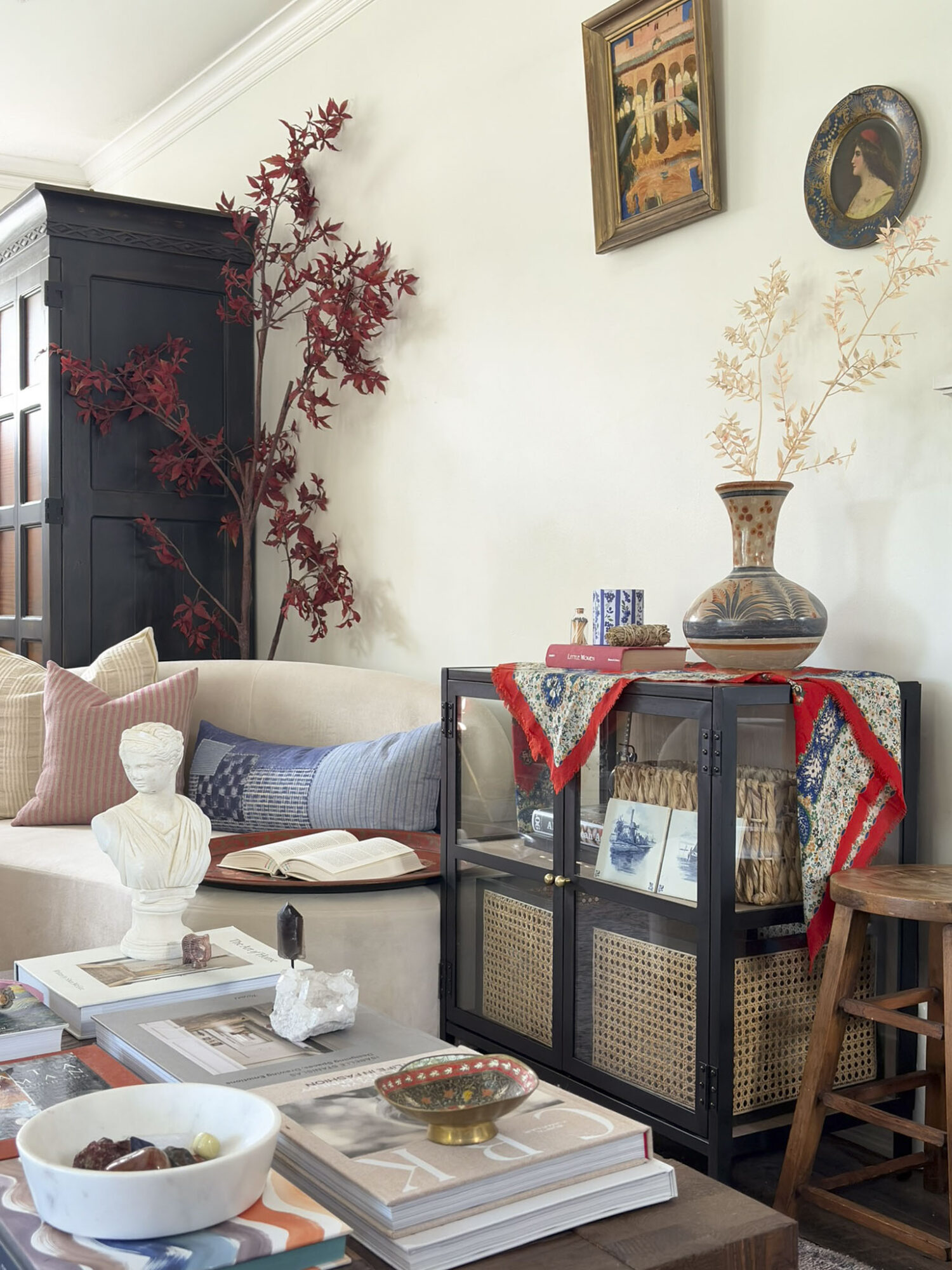 Living room with a sofa, decorative items, and wall art, featuring a black cabinet and a plant with red leaves.