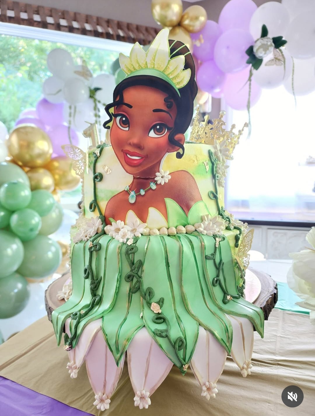 Cake with a princess character's face, green and white draped fondant, surrounded by balloons, at a celebration.