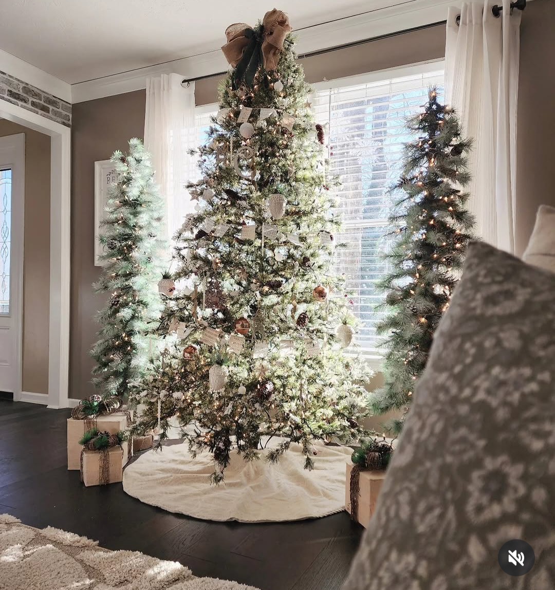 Decorated Christmas tree with presents in a living room, sunlight through window, white curtains, and a patterned pillow in foreground.