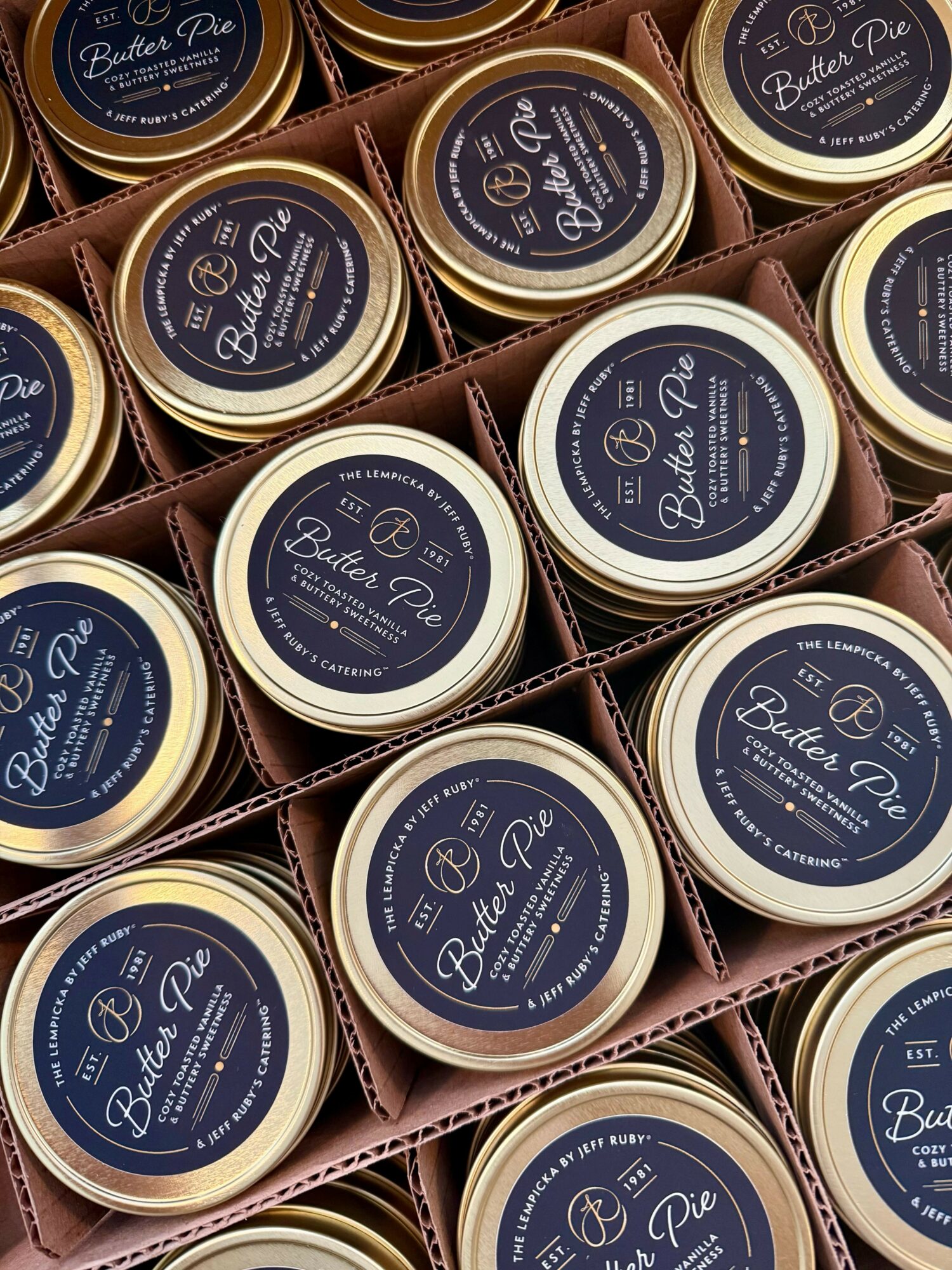 Multiple containers of butter pie with dark labels arranged in cardboard compartments.
