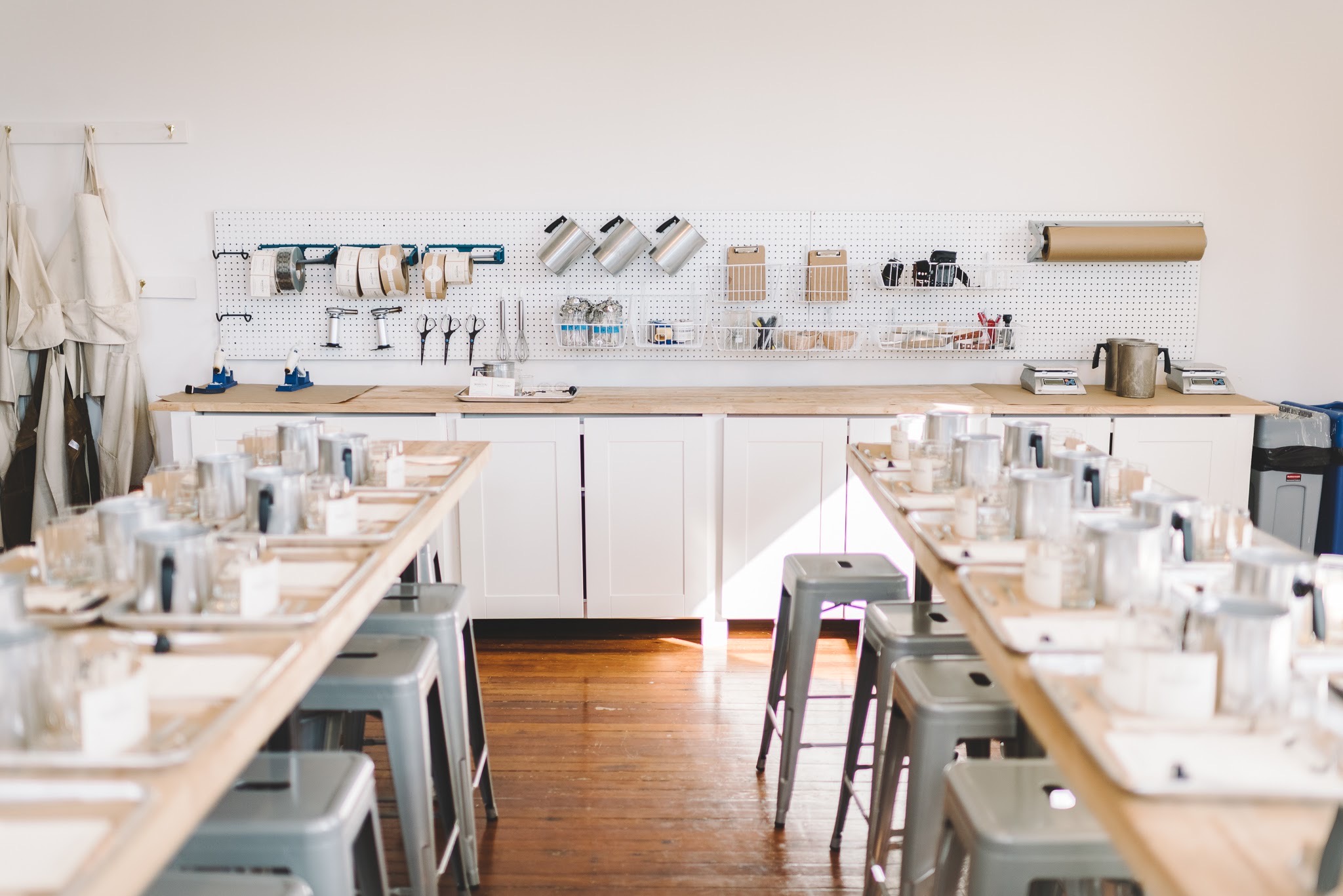 Empty dining setup with tables, chairs, and place settings in a bright room, with a wall-mounted tool and utensil storage.