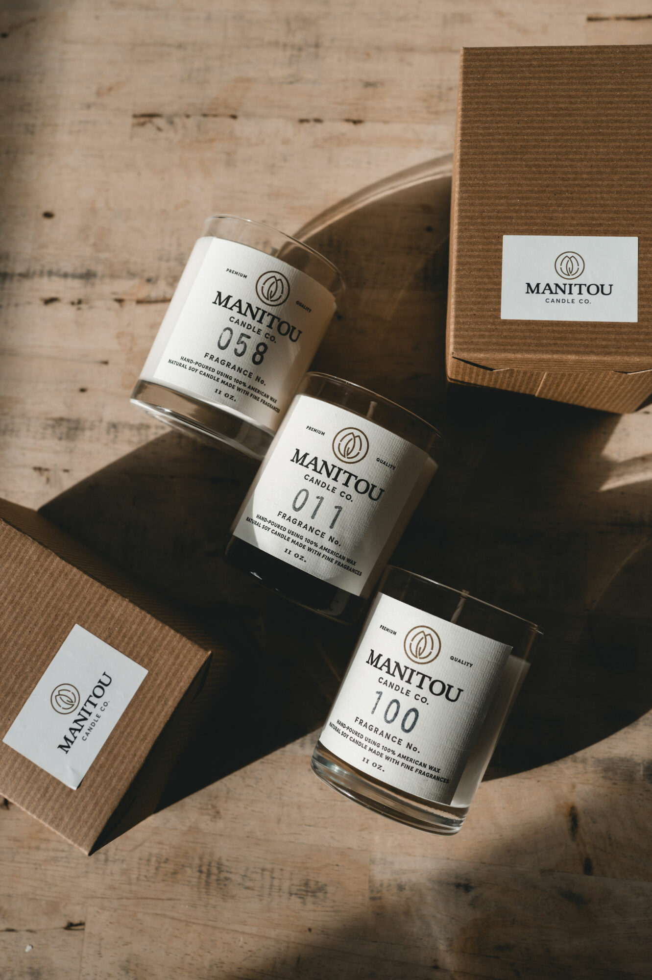 Three white candles with black labels and a brown box on a wooden surface.