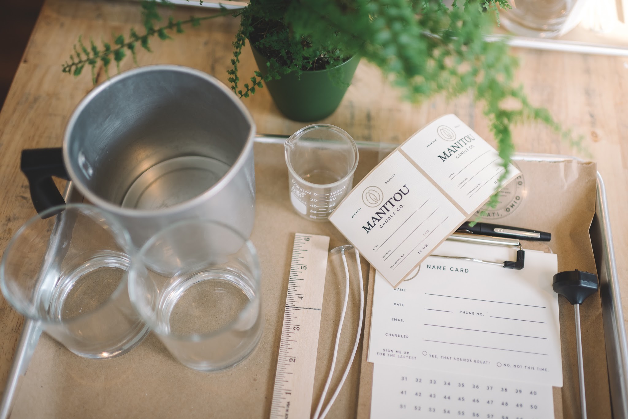 Top-down view of a wooden table with a metal bucket, glasses, a ruler, a notebook, pens, and a potted plant.