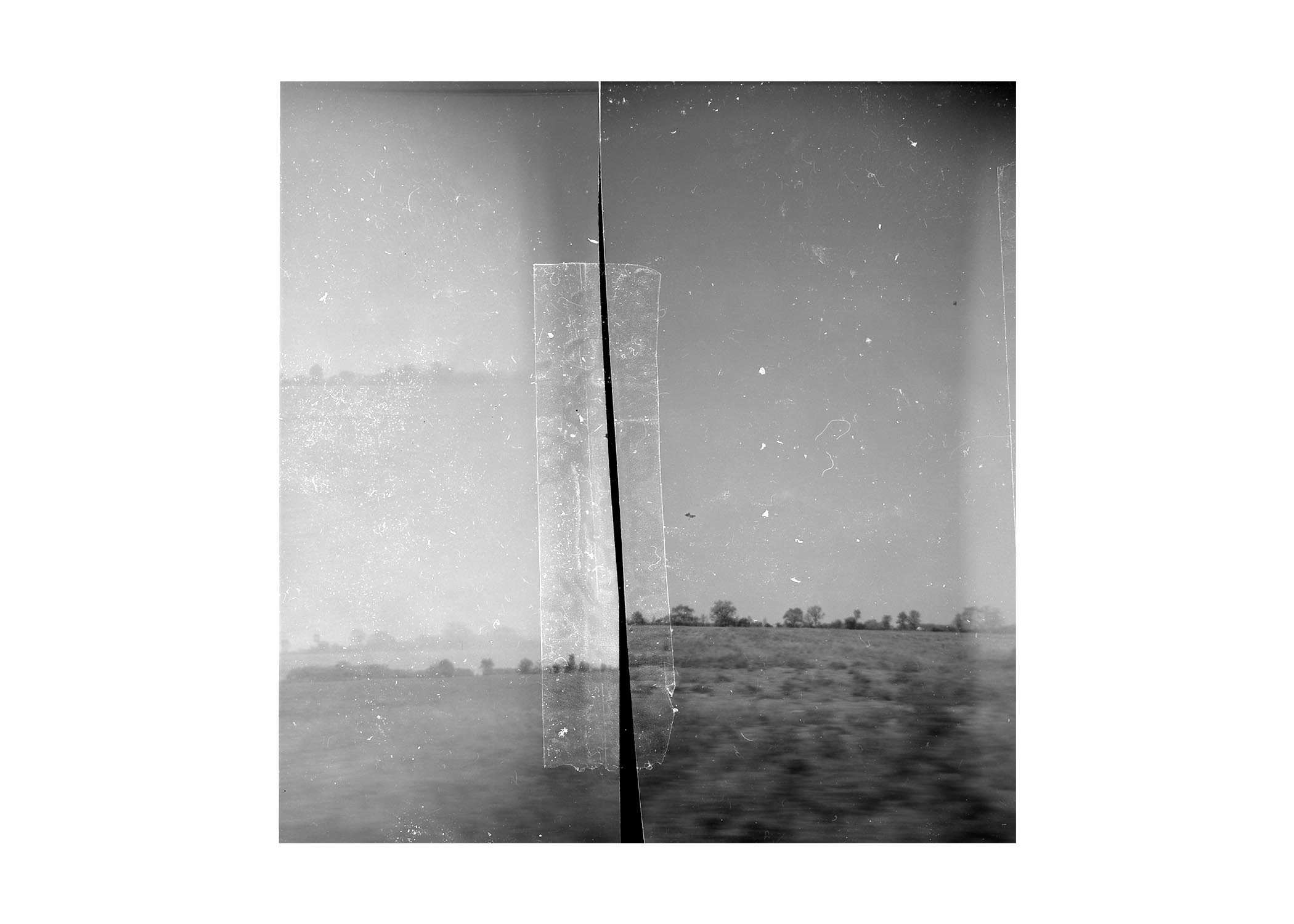 Black and white photo of a landscape with a horizon, divided by a vertical line, with sky and distant trees.
