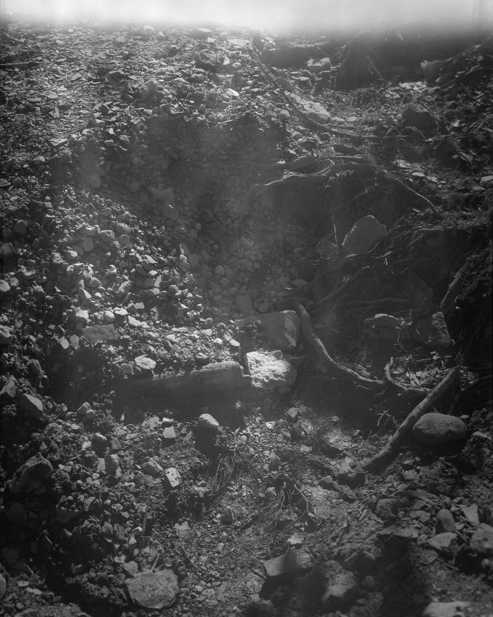 A rocky landscape with a small stream flowing through, surrounded by uneven terrain and scattered stones.