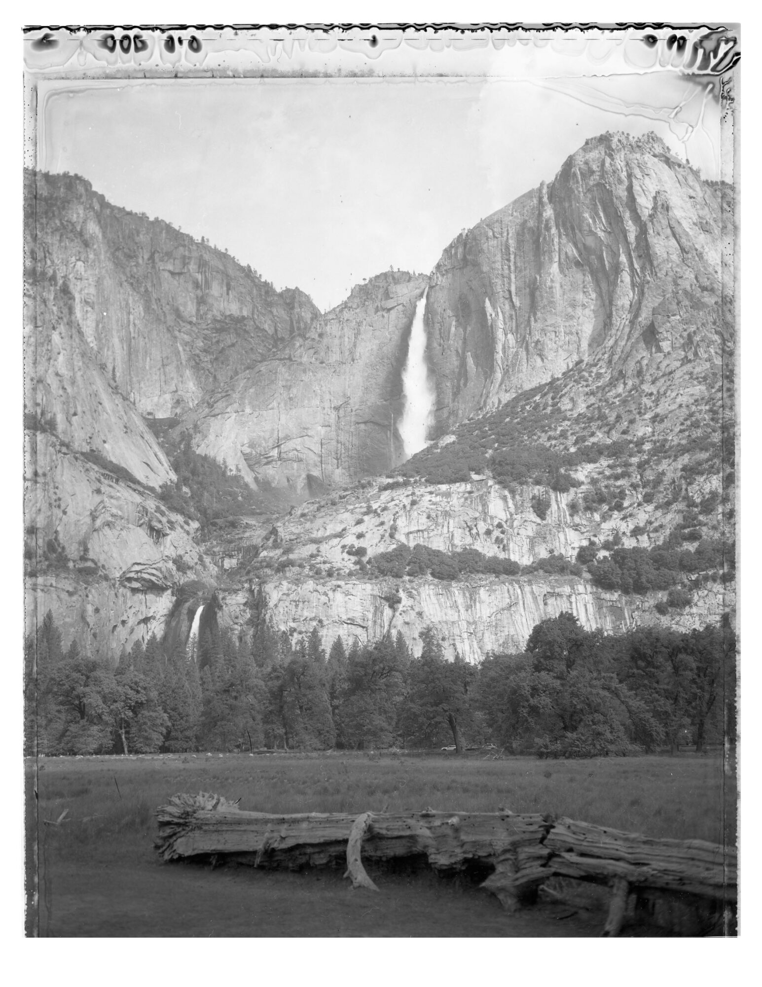 Black and white landscape with mountains, waterfalls, and a forested area in the foreground.