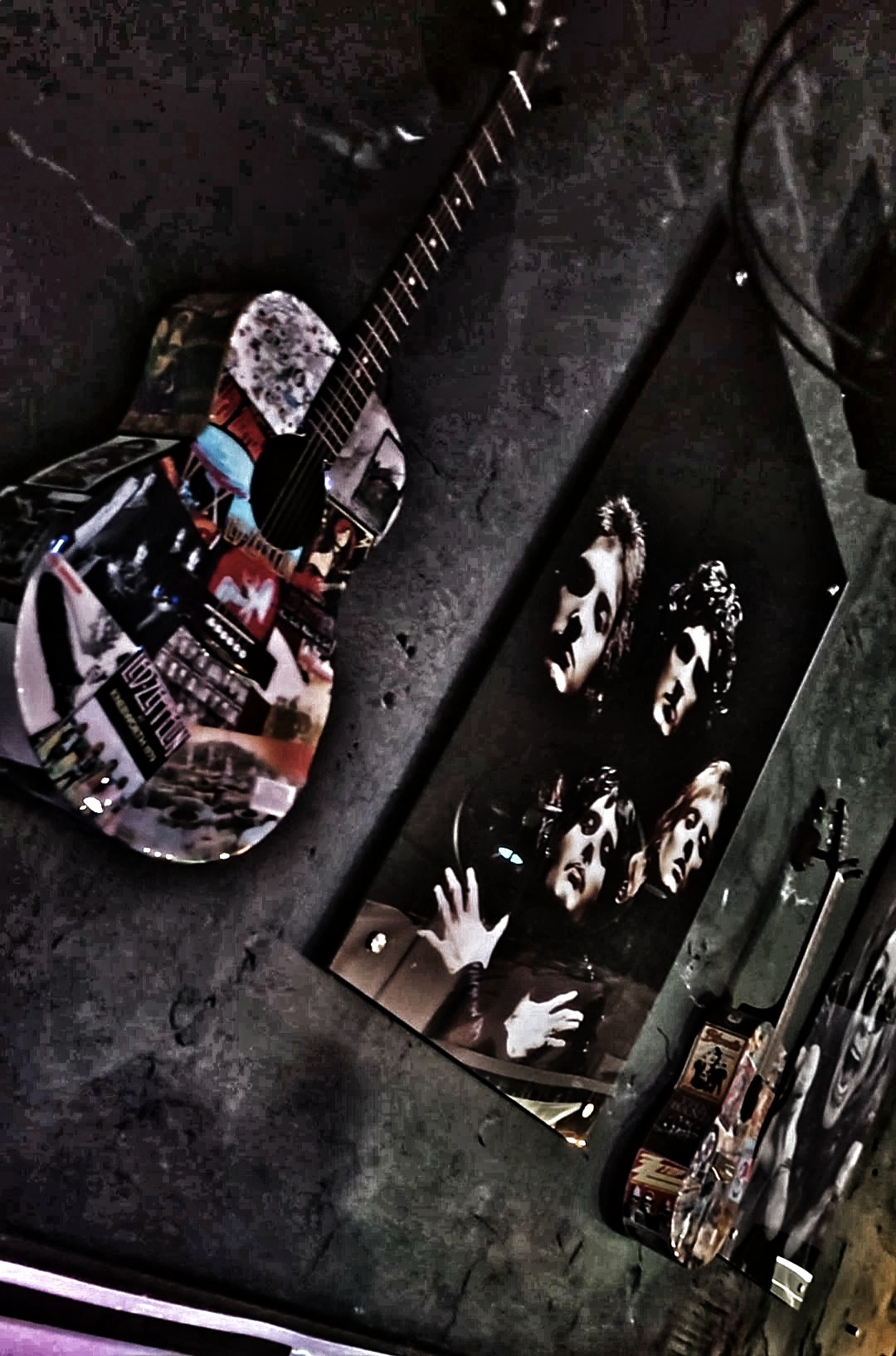 Guitar with a collage of images and a black-and-white photo of four people on a wall, with bottles nearby.