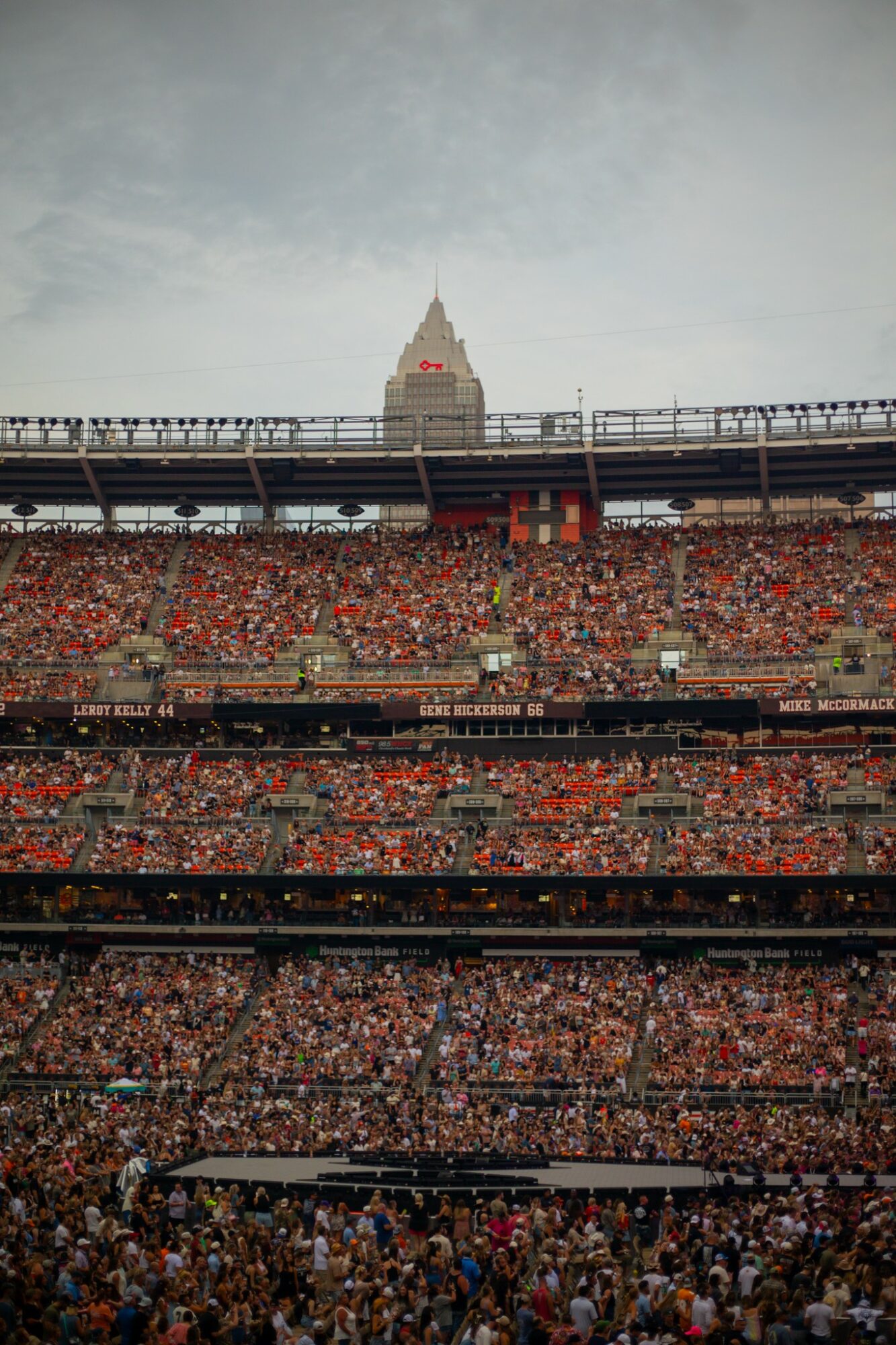 Crowd in stadium with a city building and cloudy sky in background.