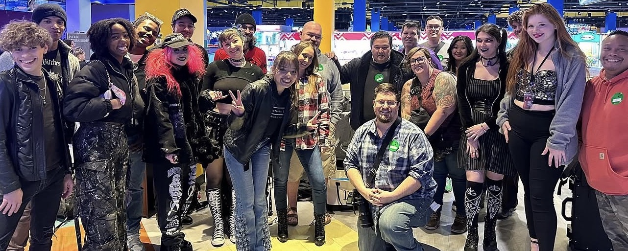 Group of people standing together indoors, some smiling and posing for the photo.