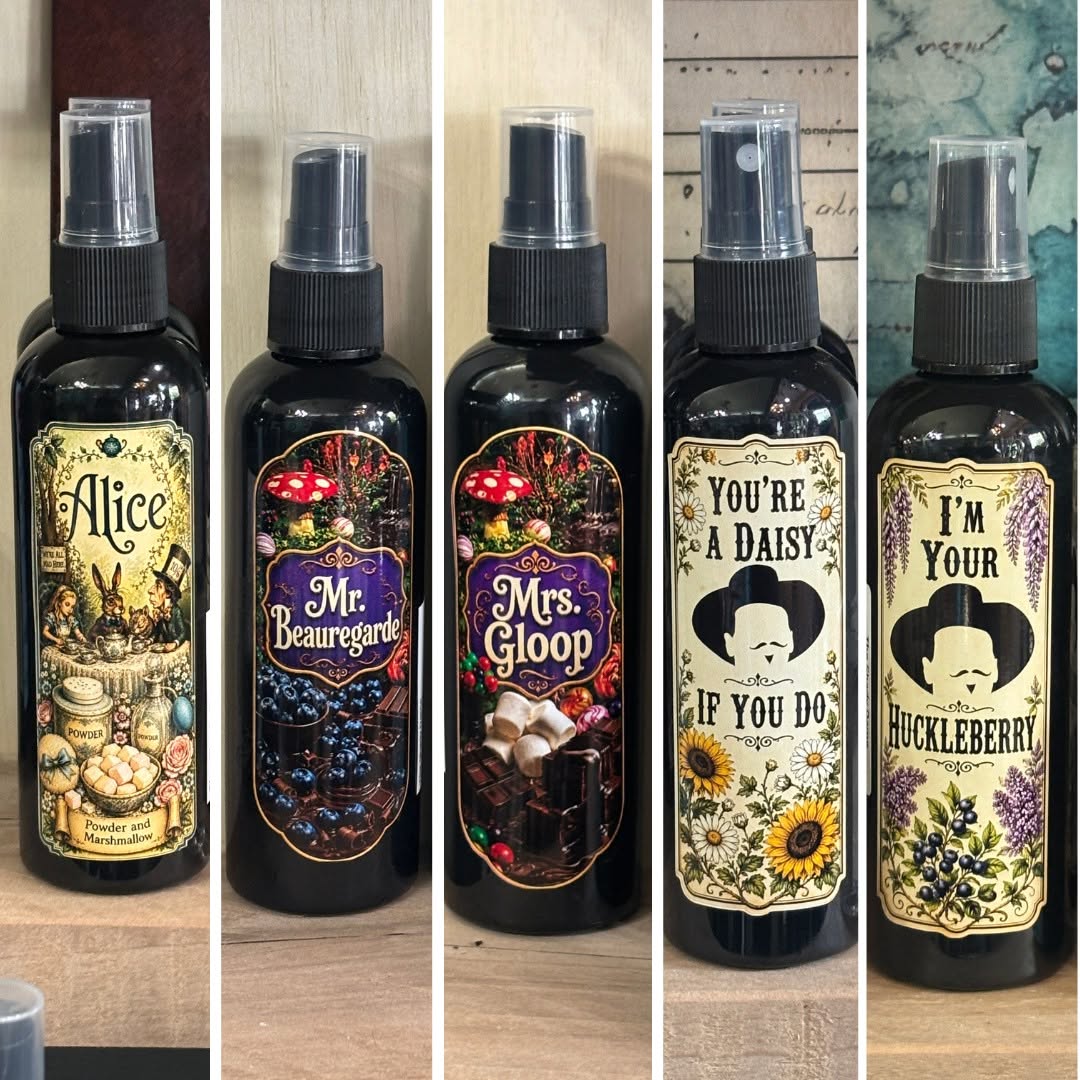 Five spray bottles with decorative labels, each featuring different designs and text, arranged in a row.