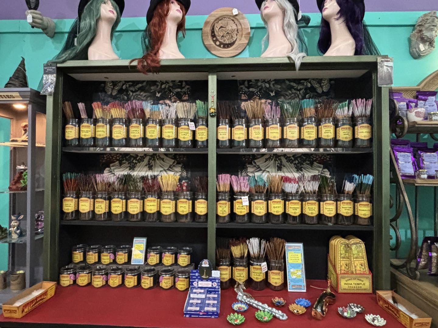 Shelves with various bottles and items, wigs on mannequins, and decorative objects on a red table, in a colorful store.