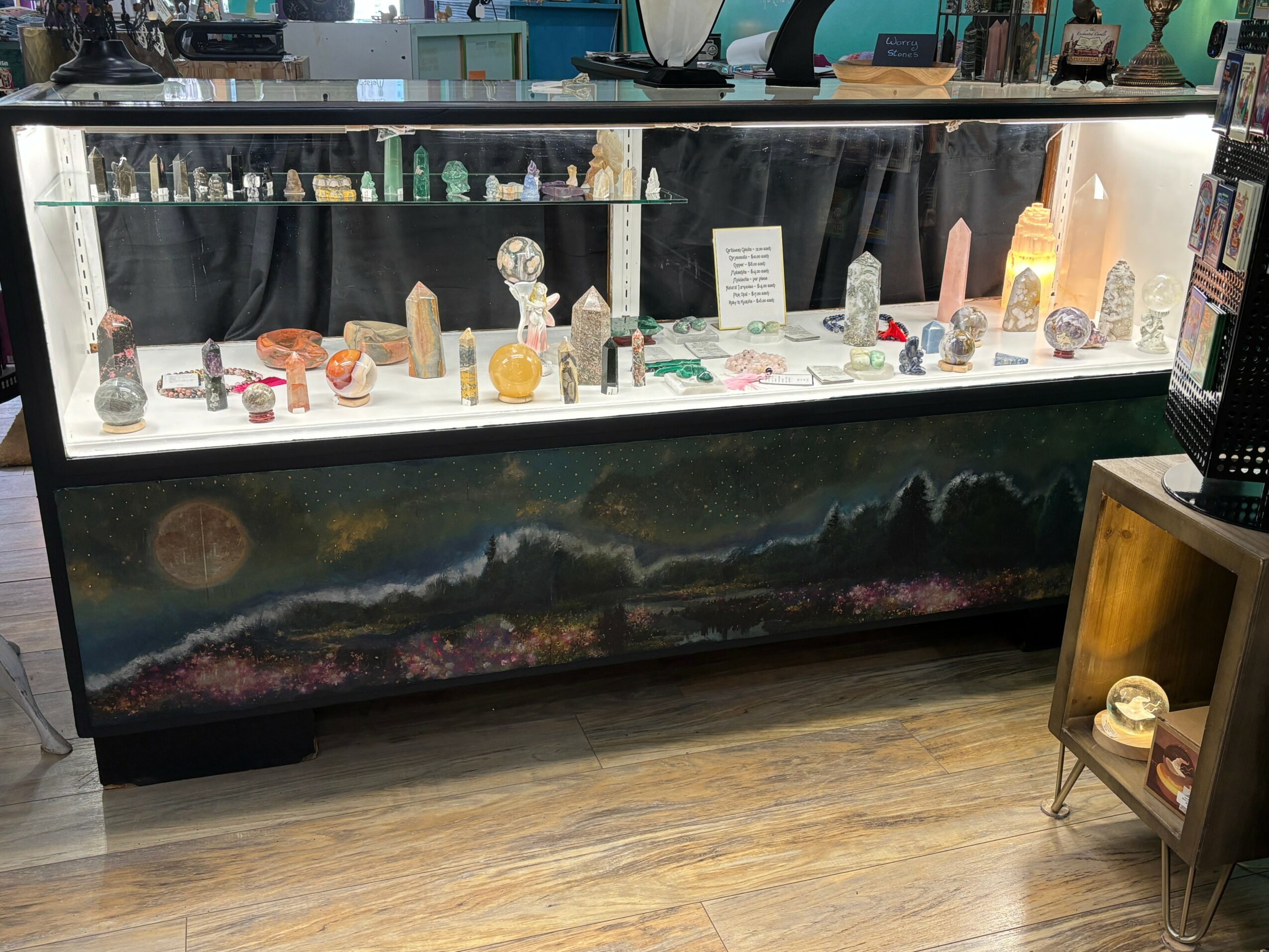 Jewelry display case with various jewelry pieces and decorative items inside, on a wooden floor.