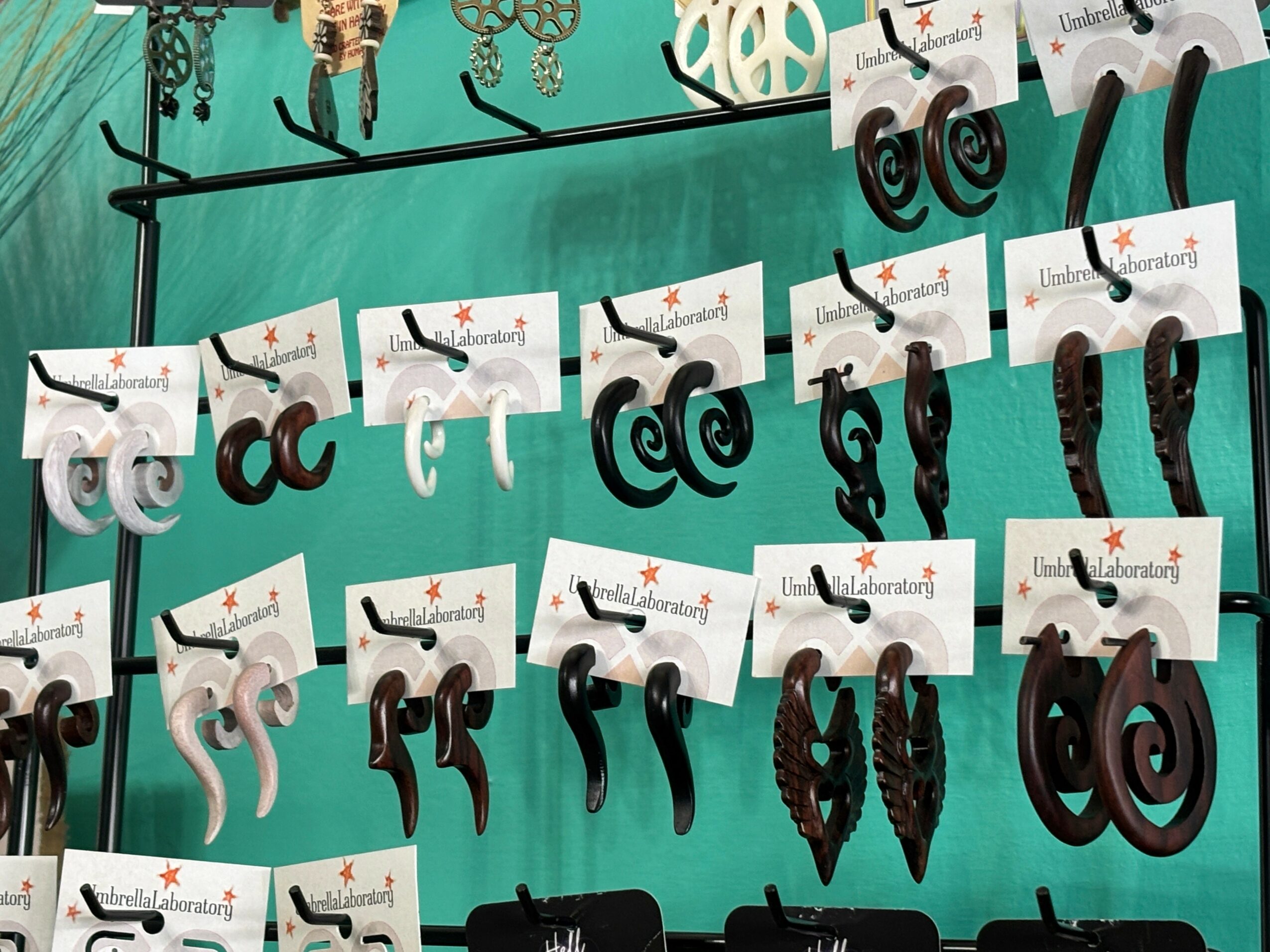 Display of black earrings on a teal background with white cards, arranged on a black rod, with some earrings hanging below.