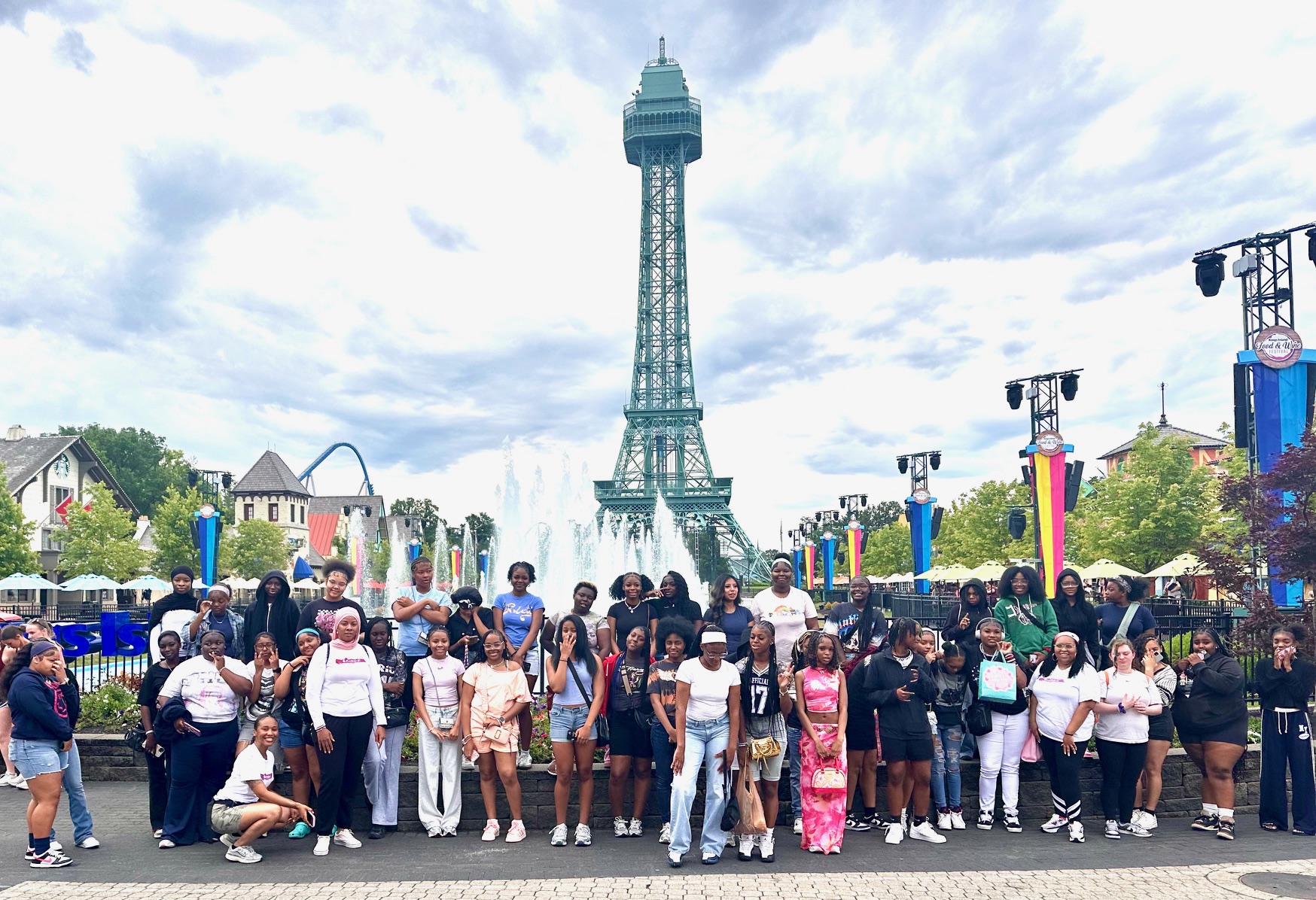 Group of people standing in front of the Eiffel Tower replica at a park, with trees and buildings in the background.