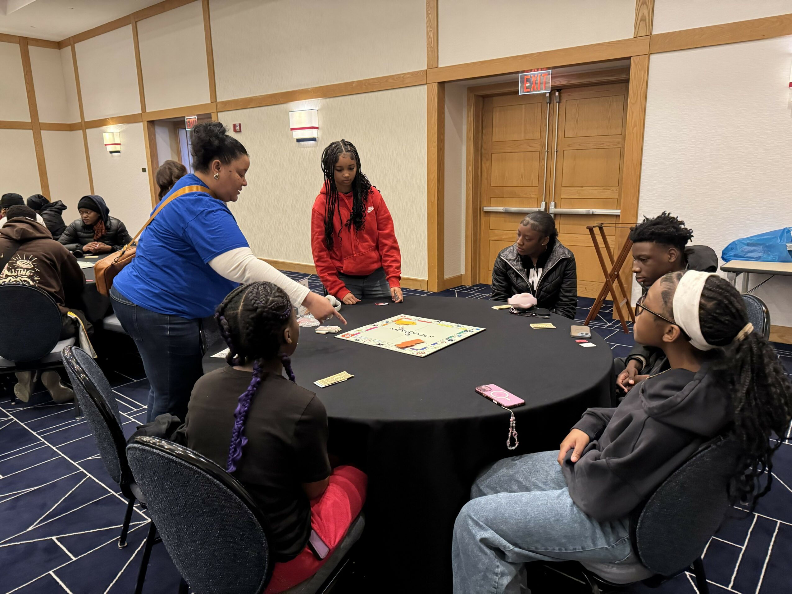 Group of people sitting around a round table in a room, with one person standing and speaking.