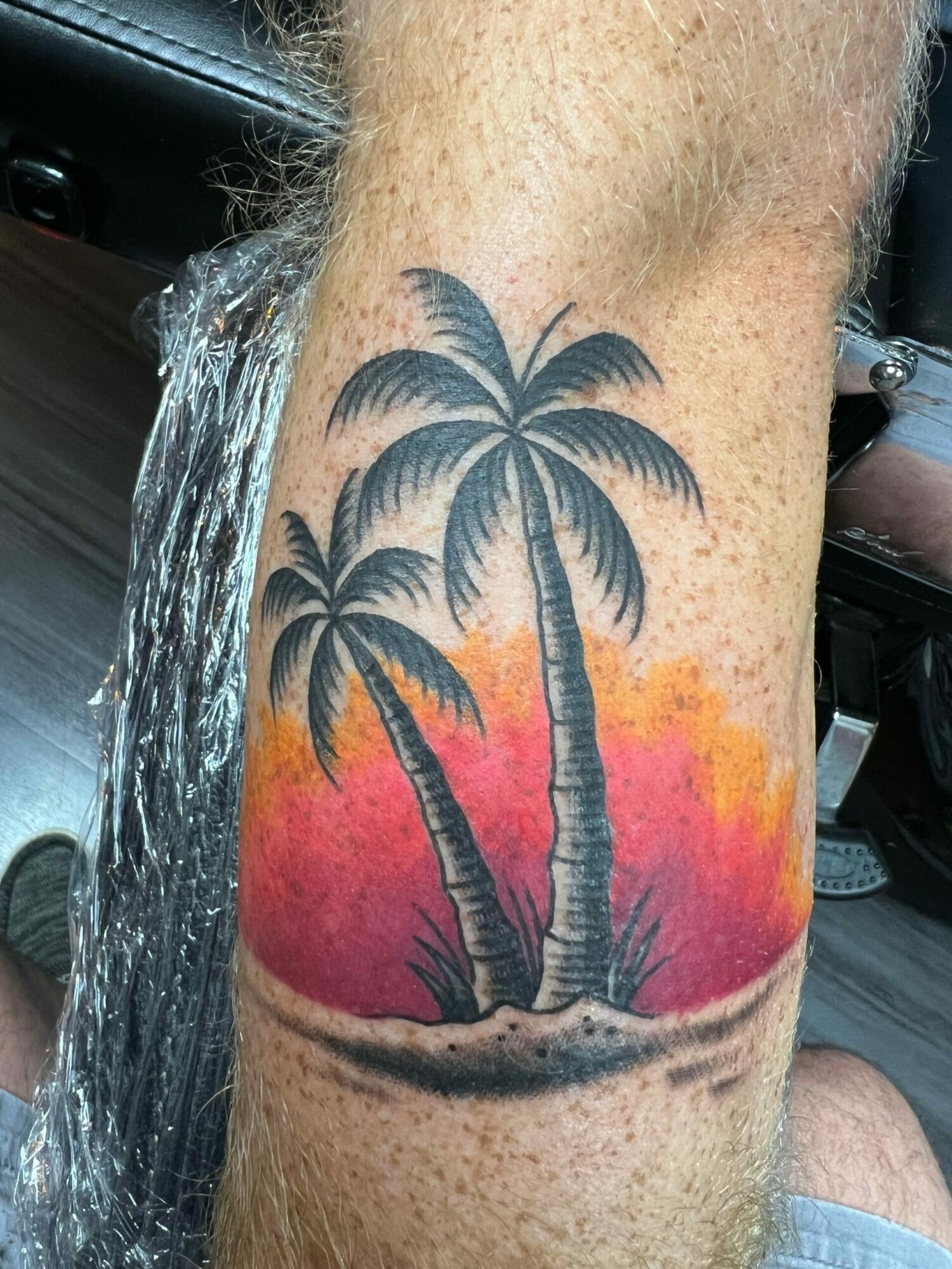 Tattoo of two palm trees on a sunset background with orange and red colors, on a person's arm.
