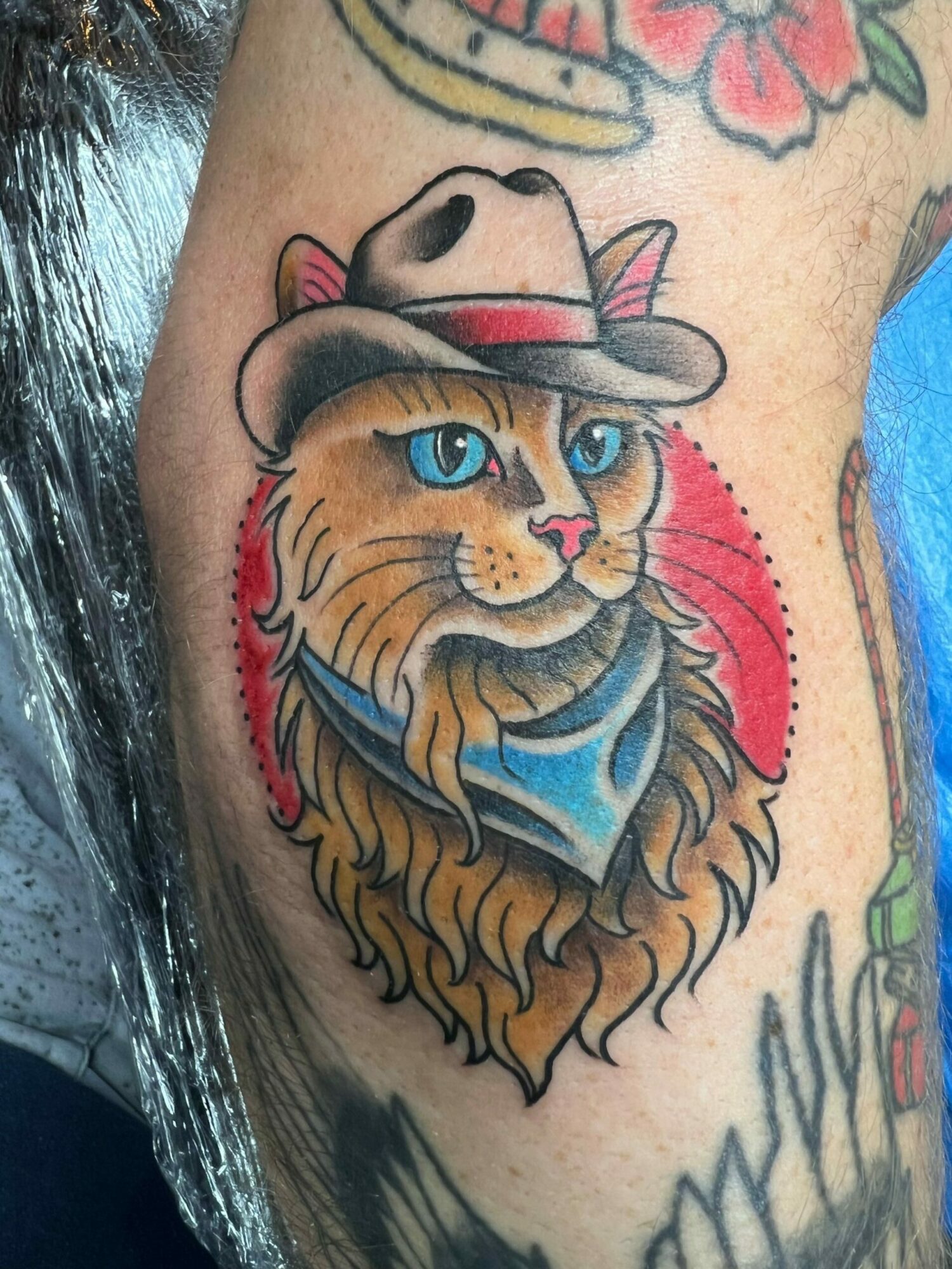 Colorful tattoo of a dog and a lion with blue eyes, wearing a blue shirt, on skin with other tattoos.