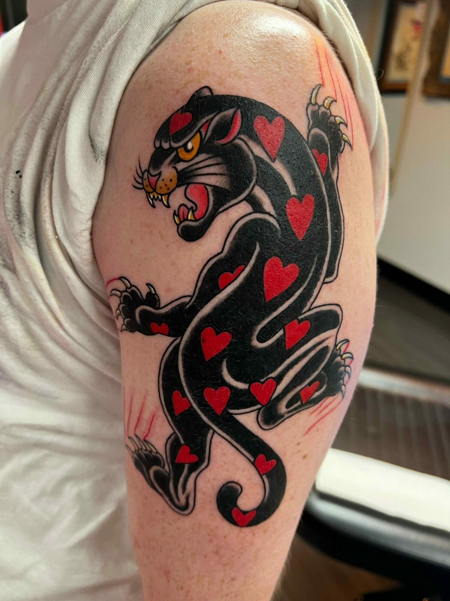 Black panther tattoo with red hearts, yellow eyes, and open mouth, on person's thigh, with skin and clothing visible.