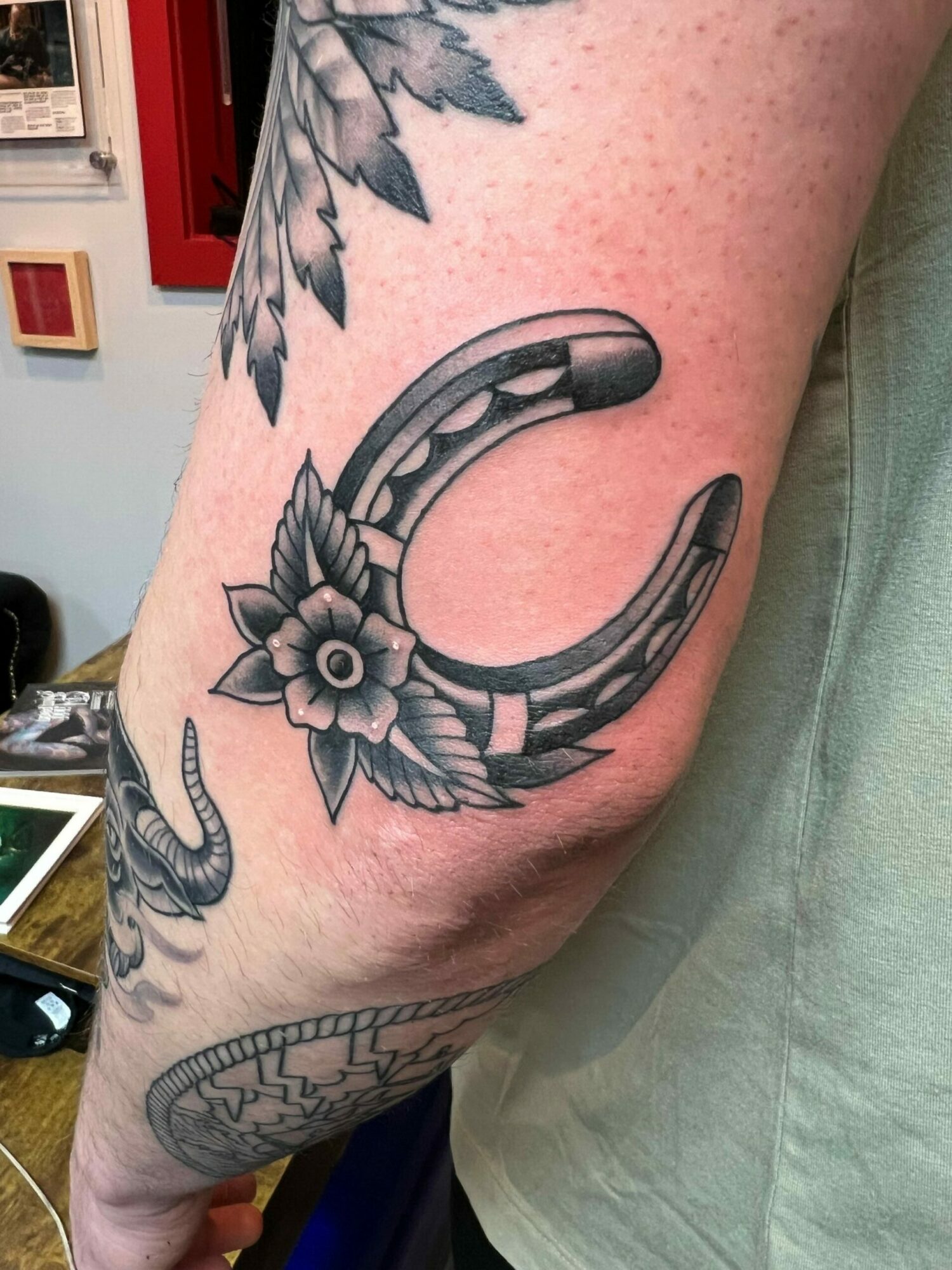 Tattoo of a crescent moon with a flower and wings on a person's arm, with a snake nearby. Bright lighting.