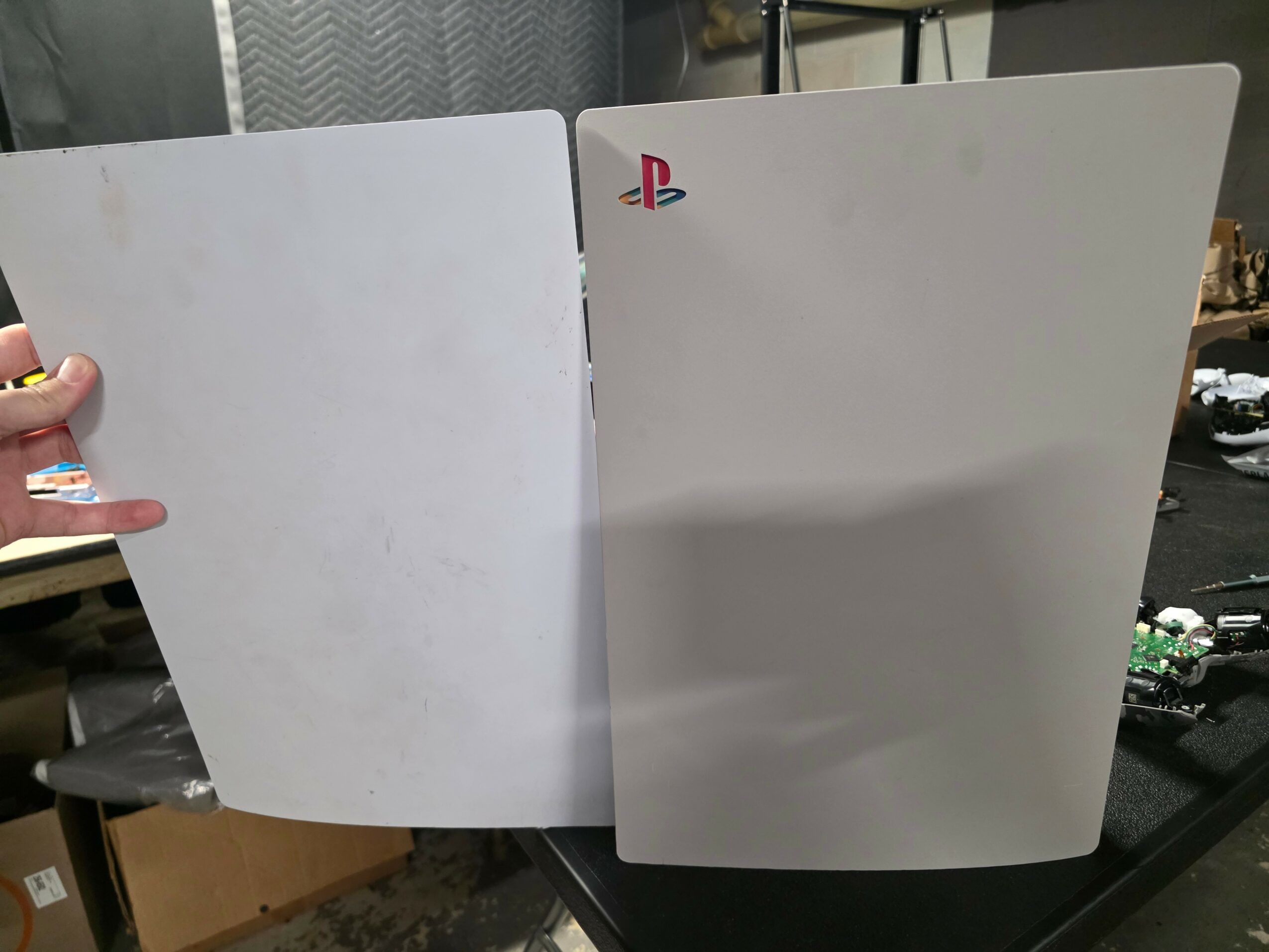 Two PlayStation 5 consoles, one with a PlayStation logo, standing upright on a table, with a person holding the left one.