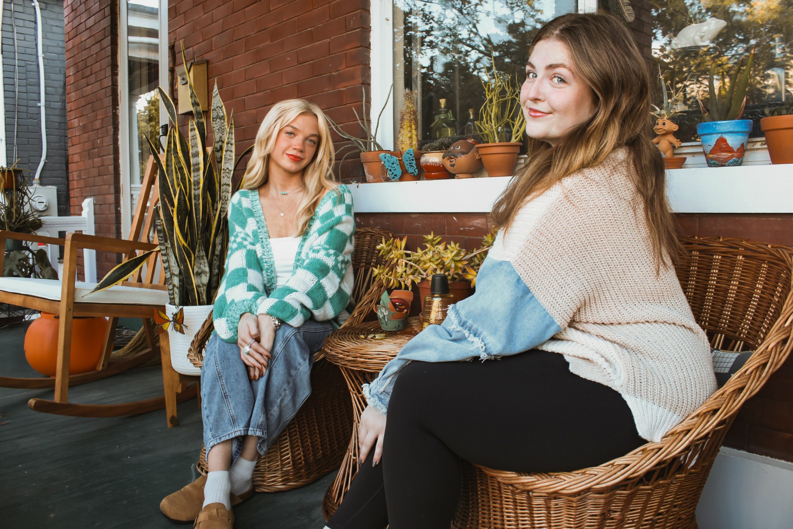 Two women sitting on a balcony with potted plants and outdoor furniture, smiling and relaxing.