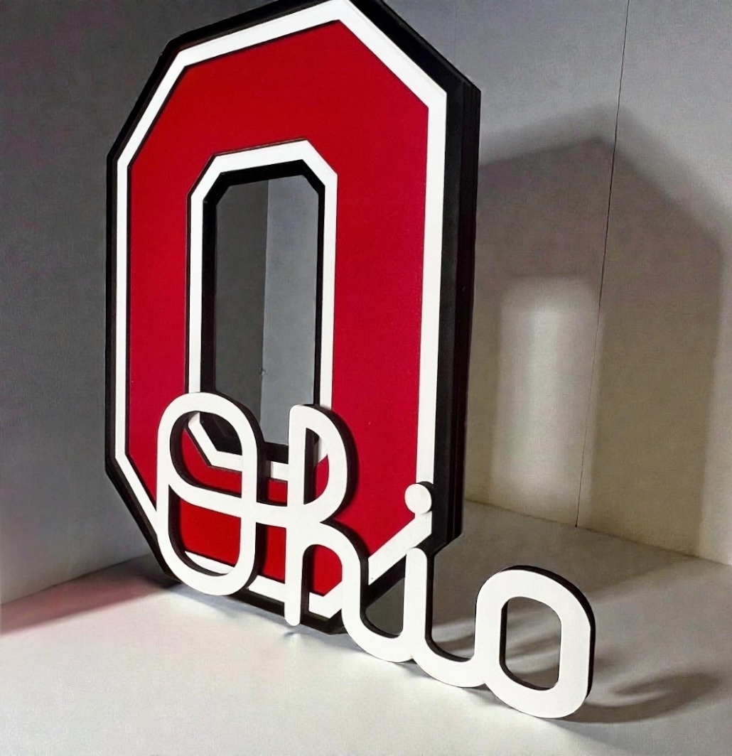 Red and white Ohio State University logo with the word 'Ohio' in white script below, placed on a surface against a wall.