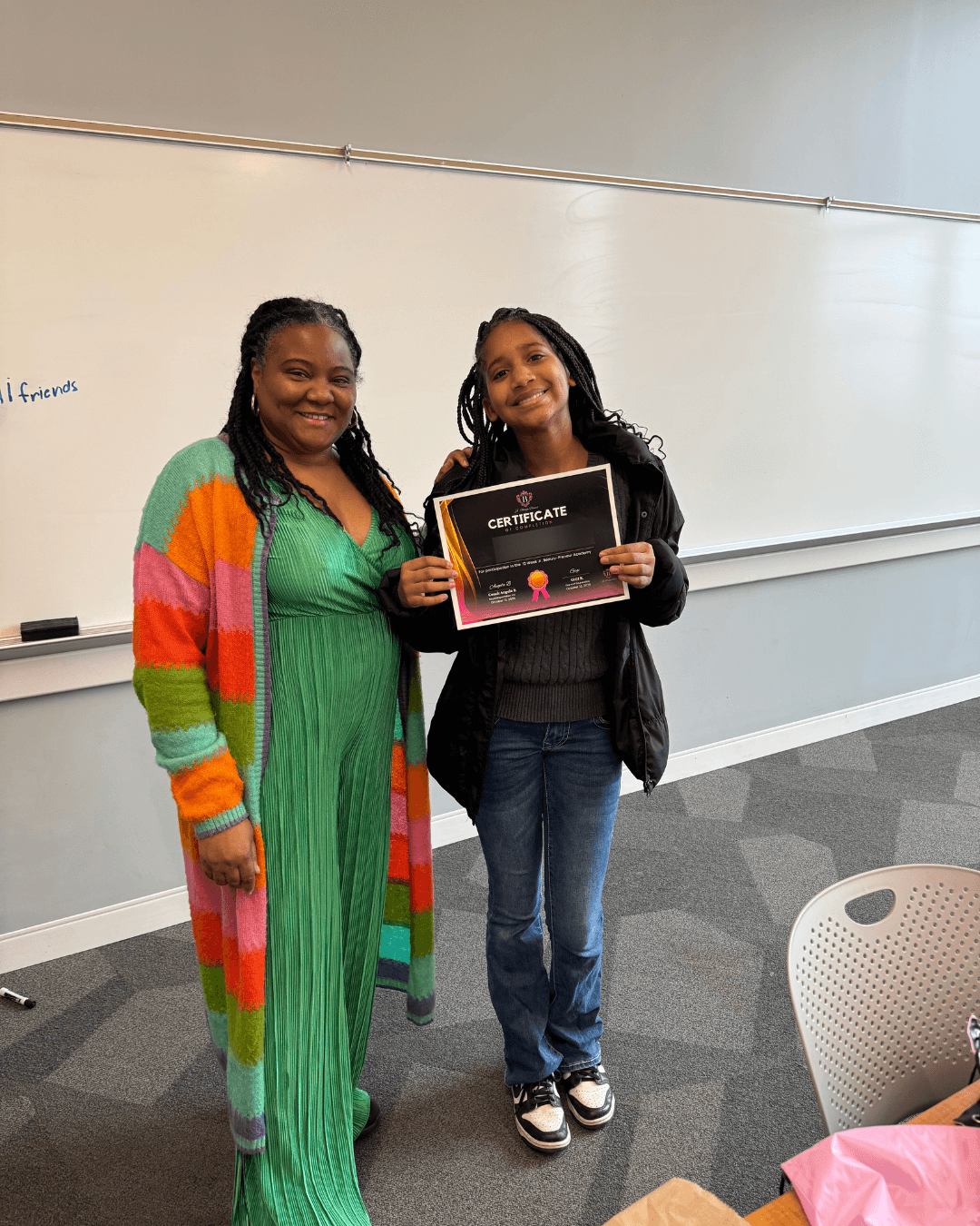 Two women standing in a classroom, one holding a certificate, smiling at the camera.